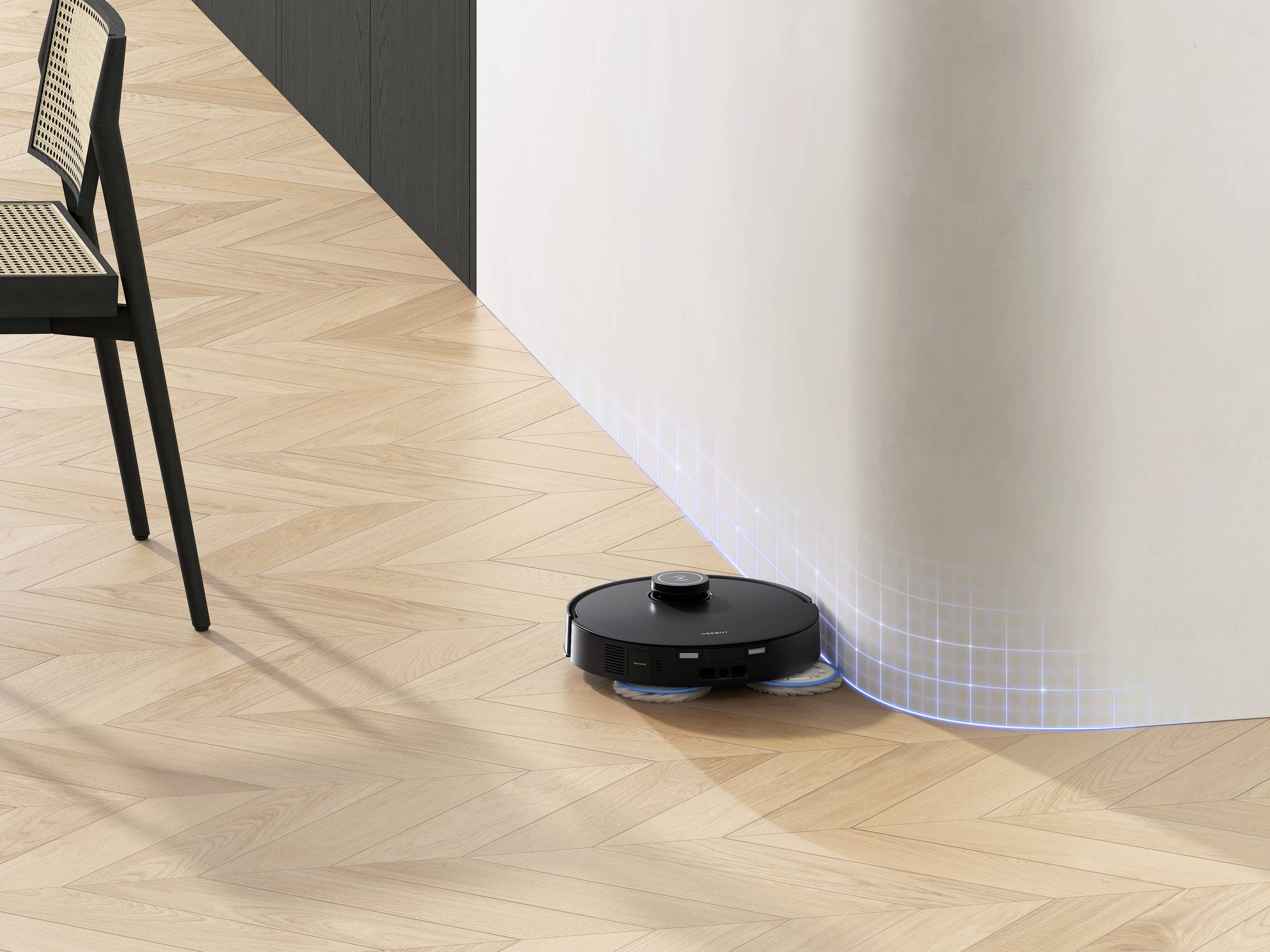 Ein schwarzer Roboterstaubsauger reinigt den Holzfußboden neben einer gebogenen Wand. Ein Stuhl steht links im Bild.