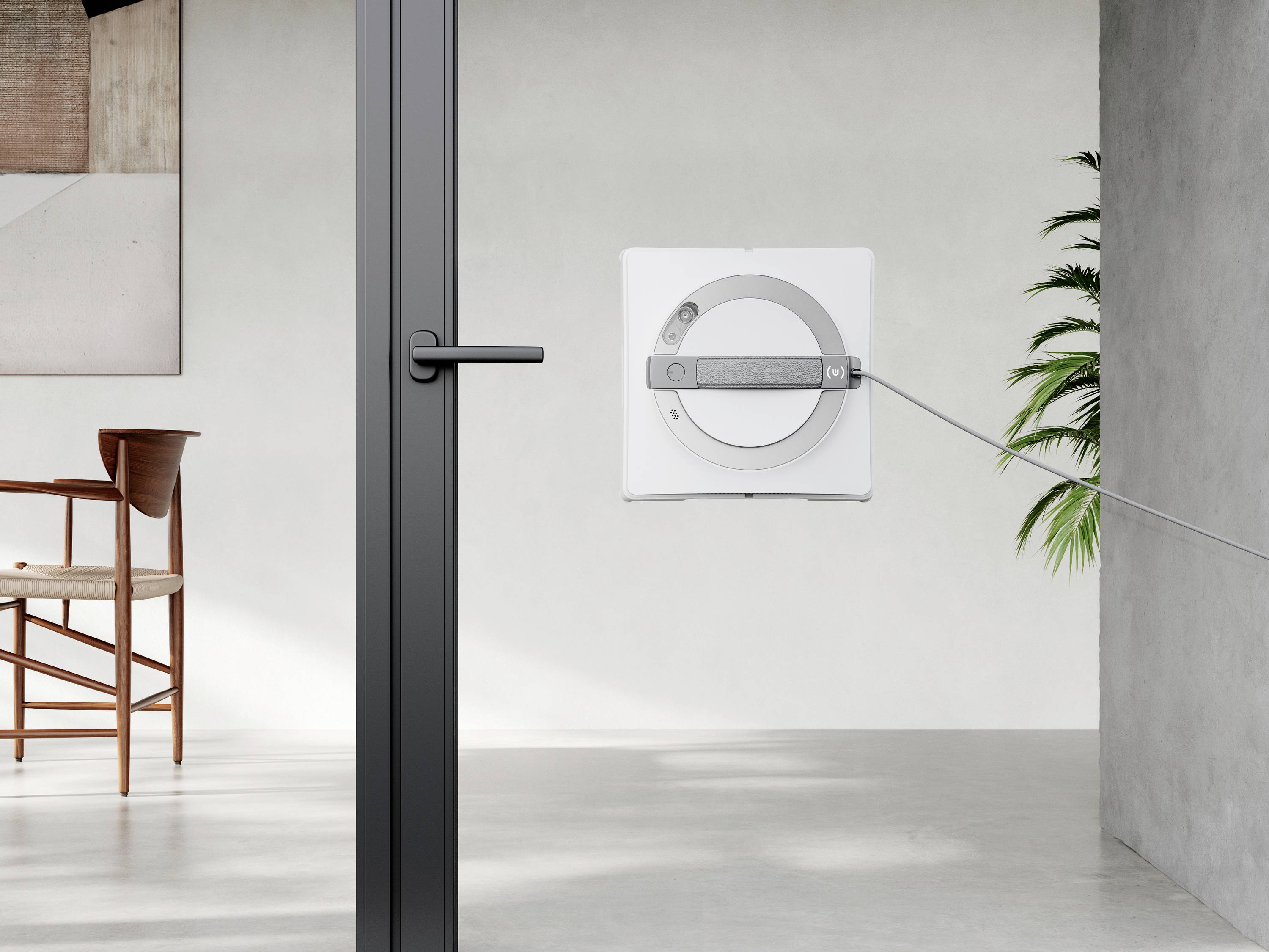 Ein quadratischer, moderner Fensterputzroboter reinigt eine große Fenstertür in einem minimalistischen Raum mit Holzmöbeln und Pflanzen.