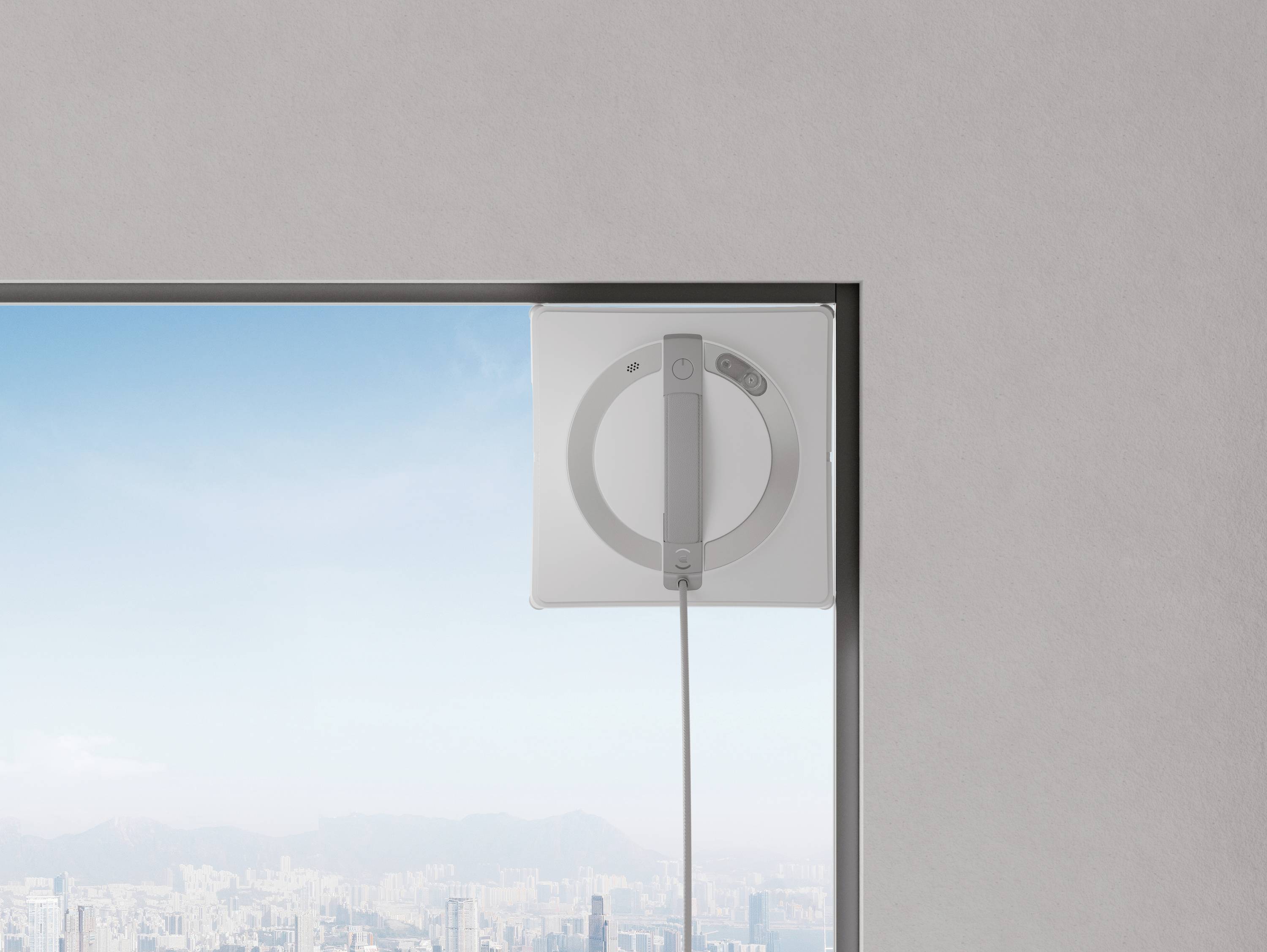 Ein Roboter zur Fensterreinigung reinigt eine große Fensterfläche mit Stadtansicht im Hintergrund, bei klarem, blauem Himmel.