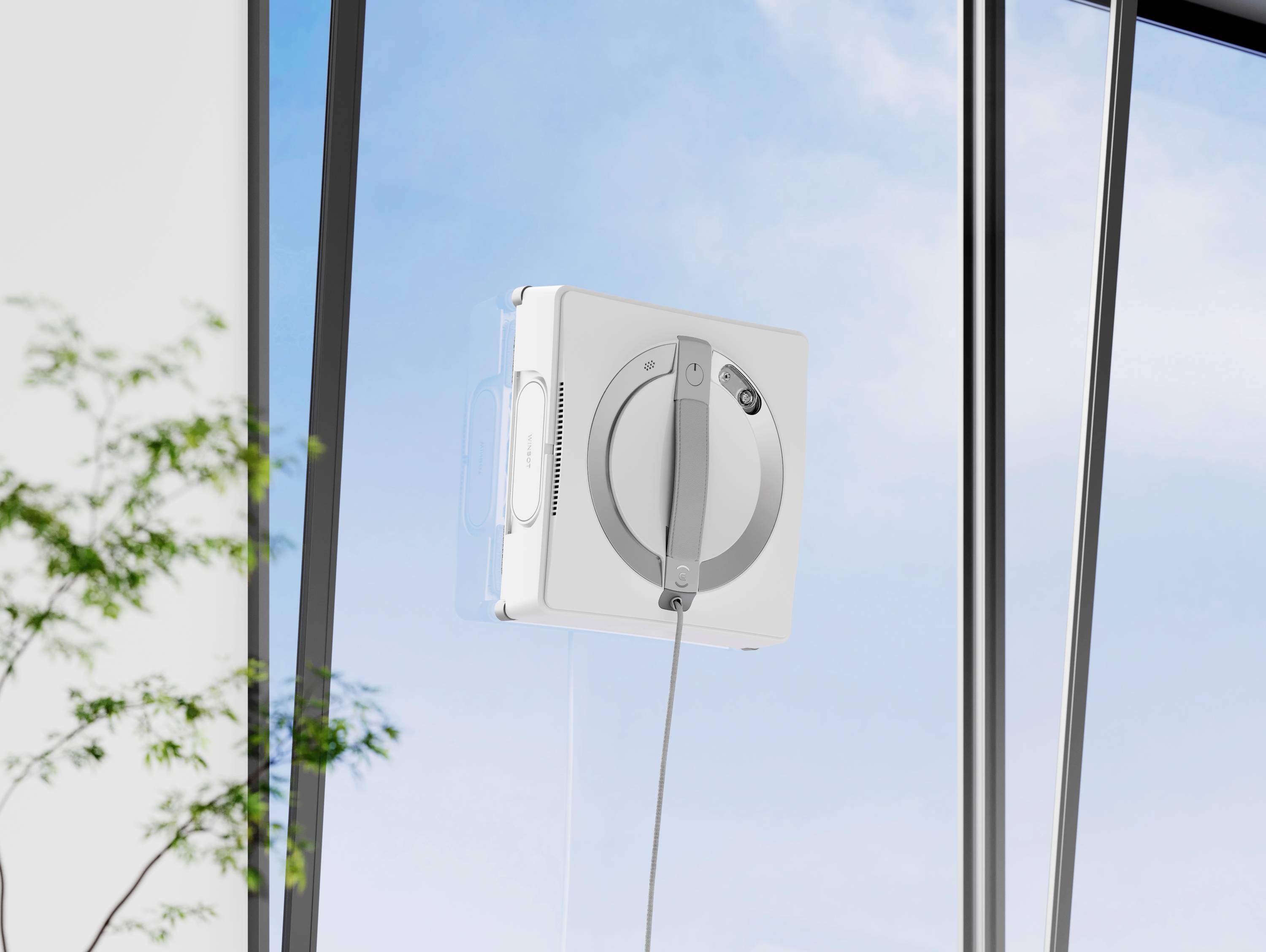 Ein quadratischer Fensterputzroboter reinigt eine große Fensterfläche; im Hintergrund ist ein klarer, blauer Himmel zu sehen.