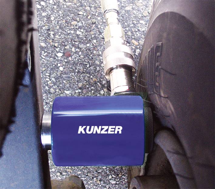Ein blaues Gerät von Kunzer ist an einem Autoreifen angeschlossen, wahrscheinlich zur Luftdruckmessung, auf einer asphaltierten Fläche.