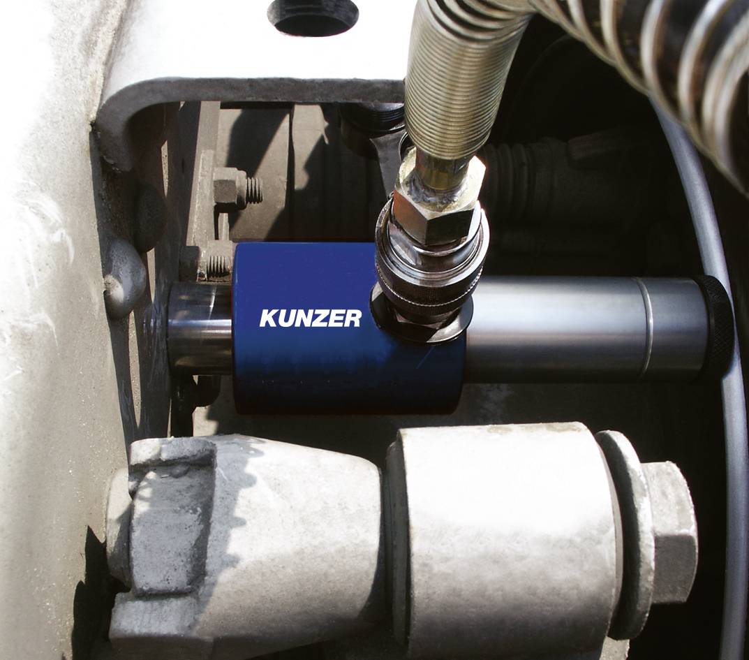 Ein Hydraulikzylinder mit einem blauen Schutzschild und der Aufschrift 'Kunzer' in einer Maschineneinheit montiert.