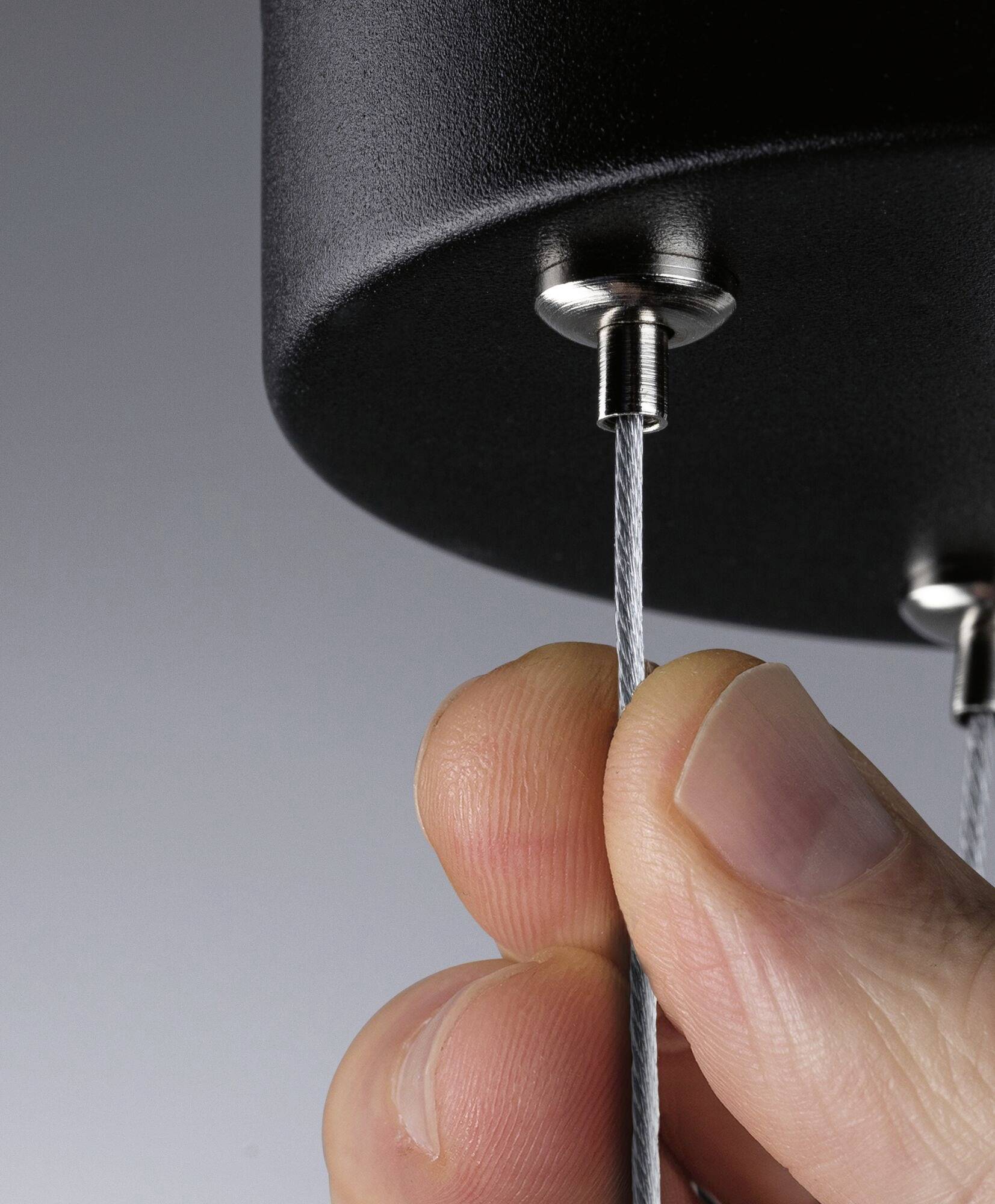 Eine Hand zieht an einem Stahlseil, das in einer Halterung befestigt ist. Der Fokus liegt auf der Spannung und Befestigung des Seils.