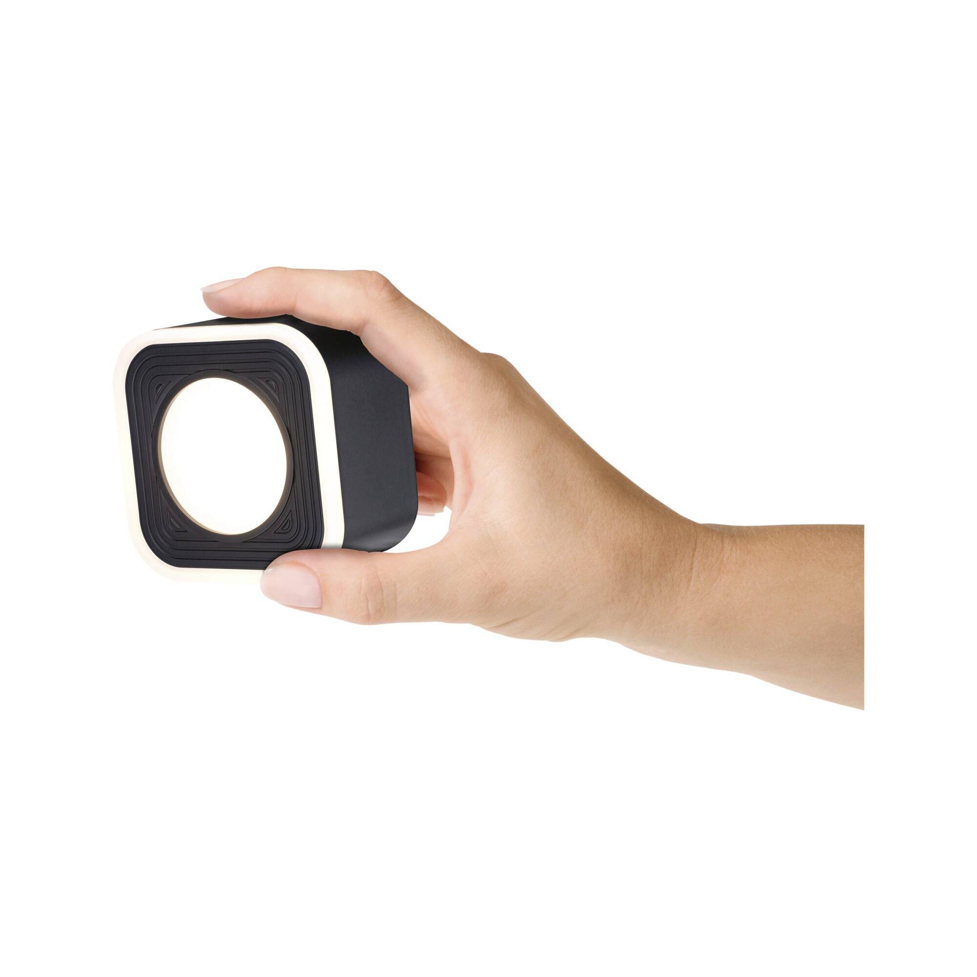 Eine Hand hält ein quadratisches Gerät mit einer runden Öffnung in der Mitte, vermutlich ein technisches Gadget oder Kamera.