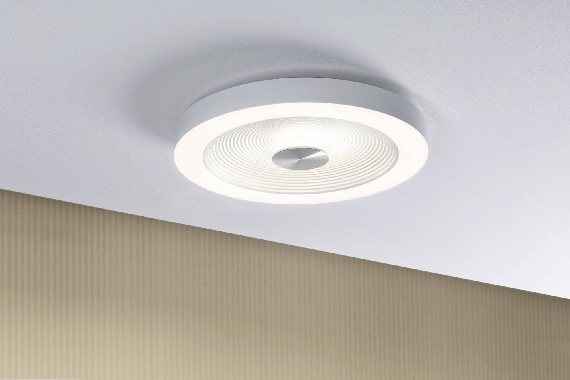 Moderne Deckenleuchte mit weißem, kreisförmigem Design leuchtet sanft von der Decke. Hintergrund zeigt eine beige Wand.