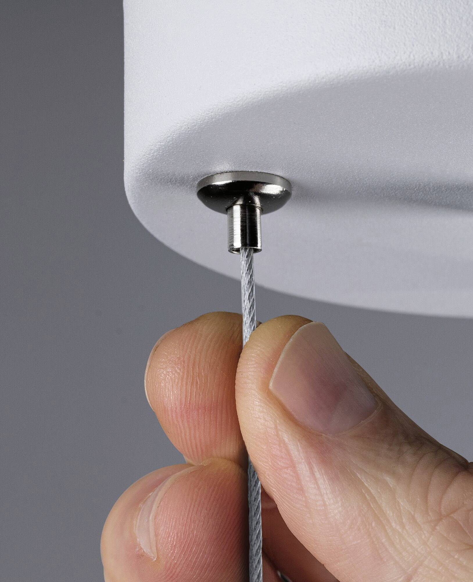 Eine Hand hält ein Metallseil, das an einem runden, weißen Objekt befestigt ist. Der Fokus liegt auf der Verbindung des Seils.