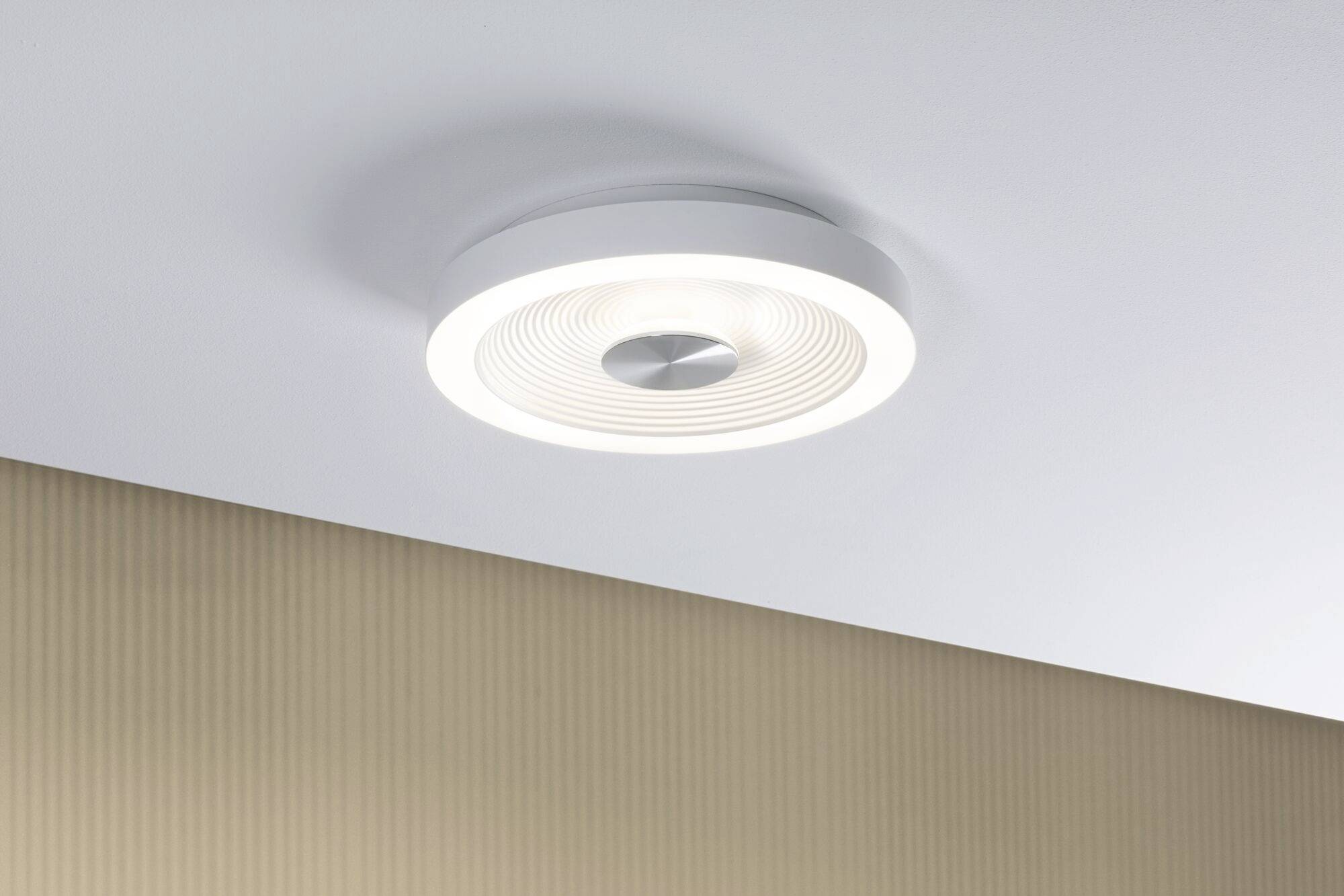 Deckenleuchte mit modernem, rundem Design, strahlt angenehmes weißes Licht aus. Lampe an weißer Decke über beigem, geripptem Hintergrund.