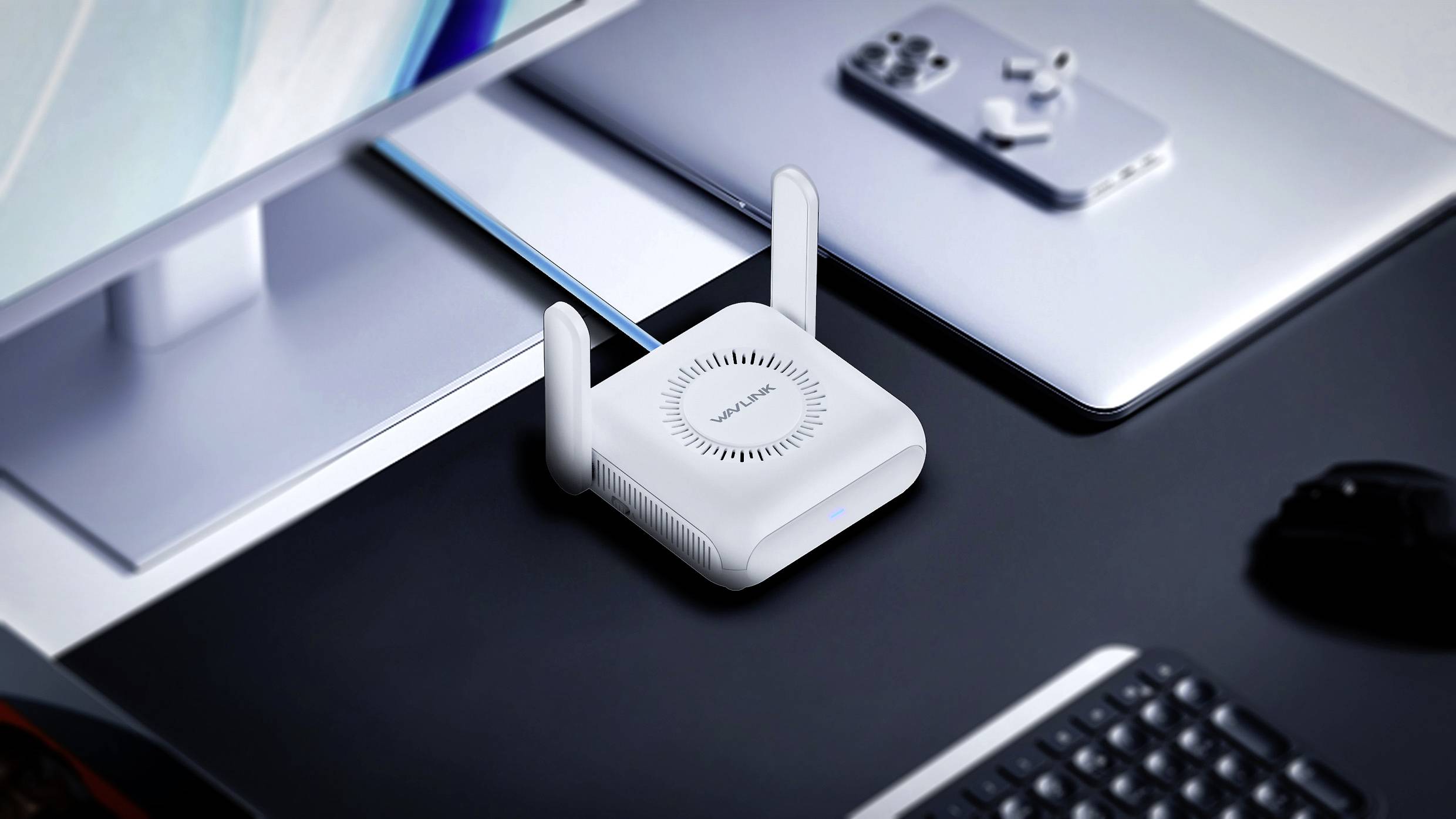 Ein weißer WLAN-Router mit zwei Antennen steht auf einem Schreibtisch neben einem Laptop, einer Tastatur und einem Monitor.