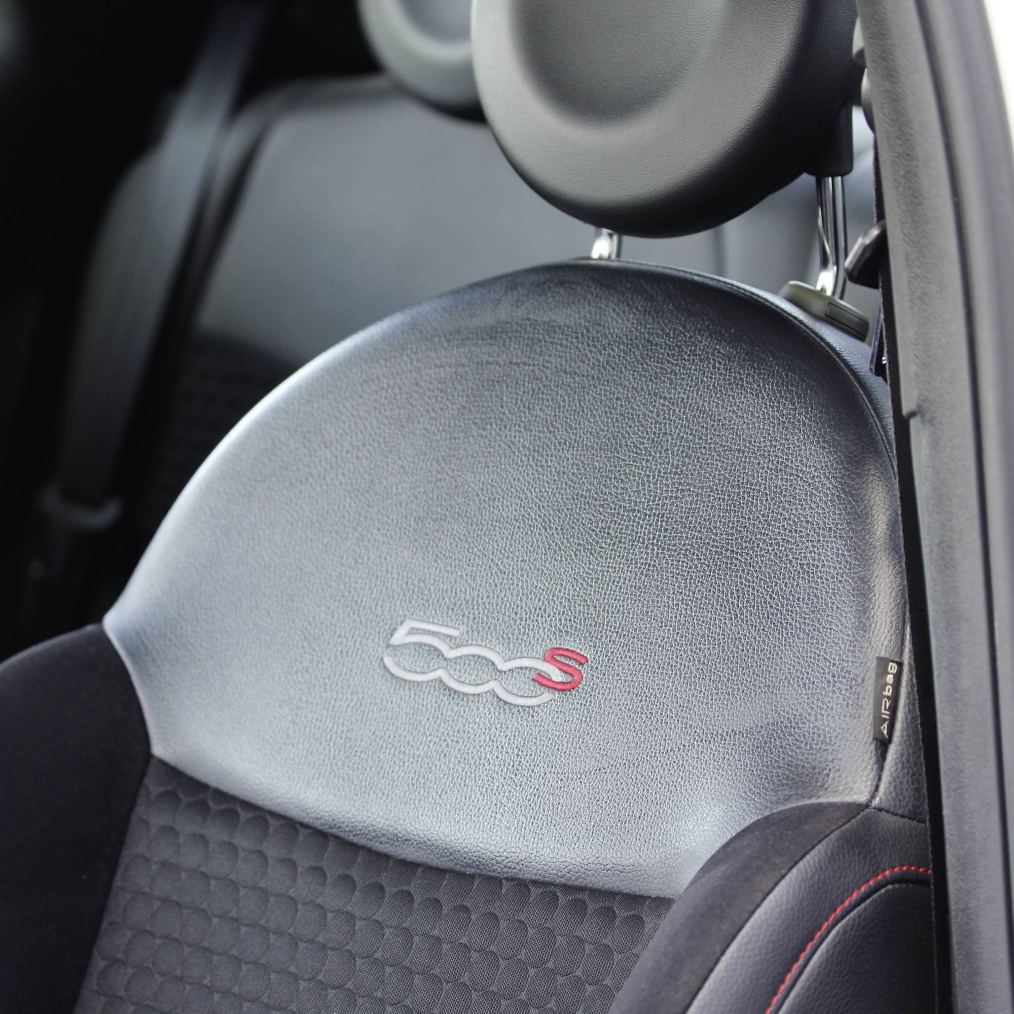 Autositz eines Fiat 500S mit schwarzem Stoff und eingeprägtem '500S'-Emblem auf der Rückenlehne, Seitenansicht des Fahrzeugsitzes.