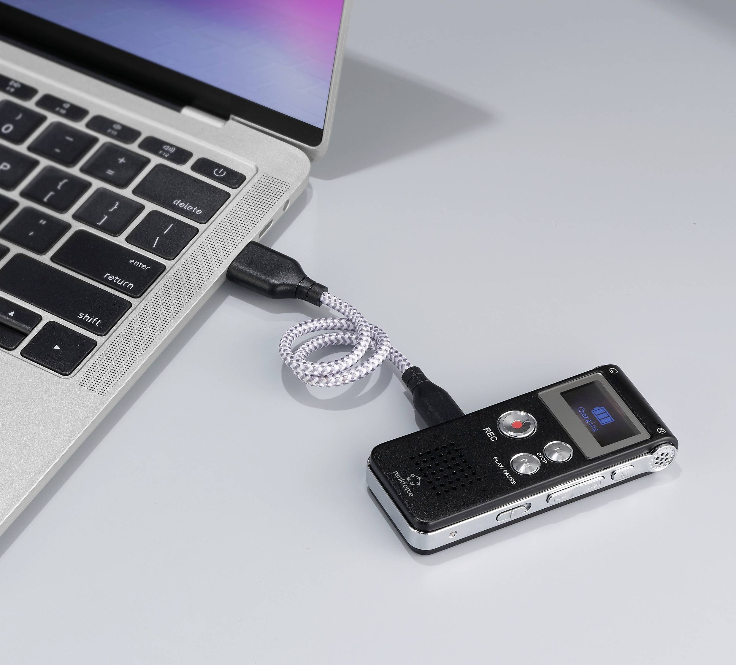 Ein Diktiergerät ist über ein USB-Kabel mit einem Laptop verbunden. Das Display des Diktiergeräts zeigt '001'.