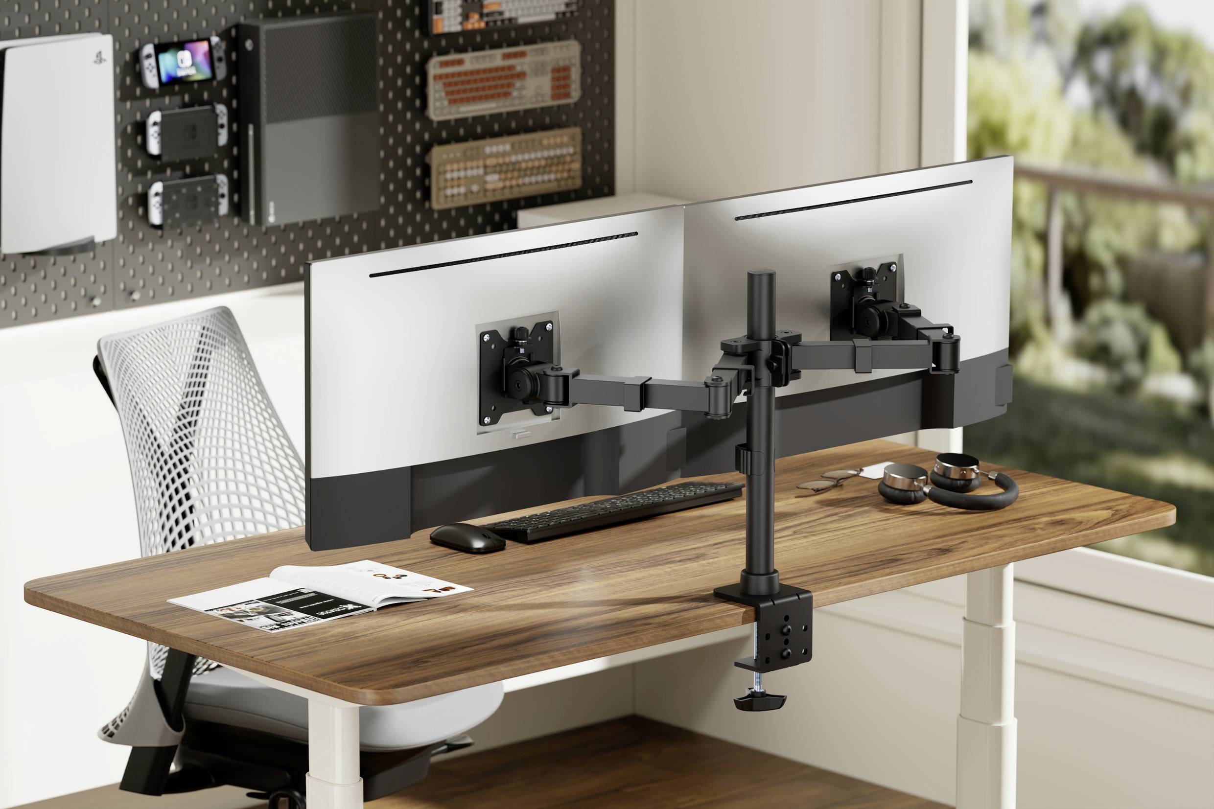 Ein Schreibtisch mit zwei Monitoren auf Halterungen, Tastatur, Maus und einem Laptopständer. Im Hintergrund ein Fenster mit Blick ins Freie.