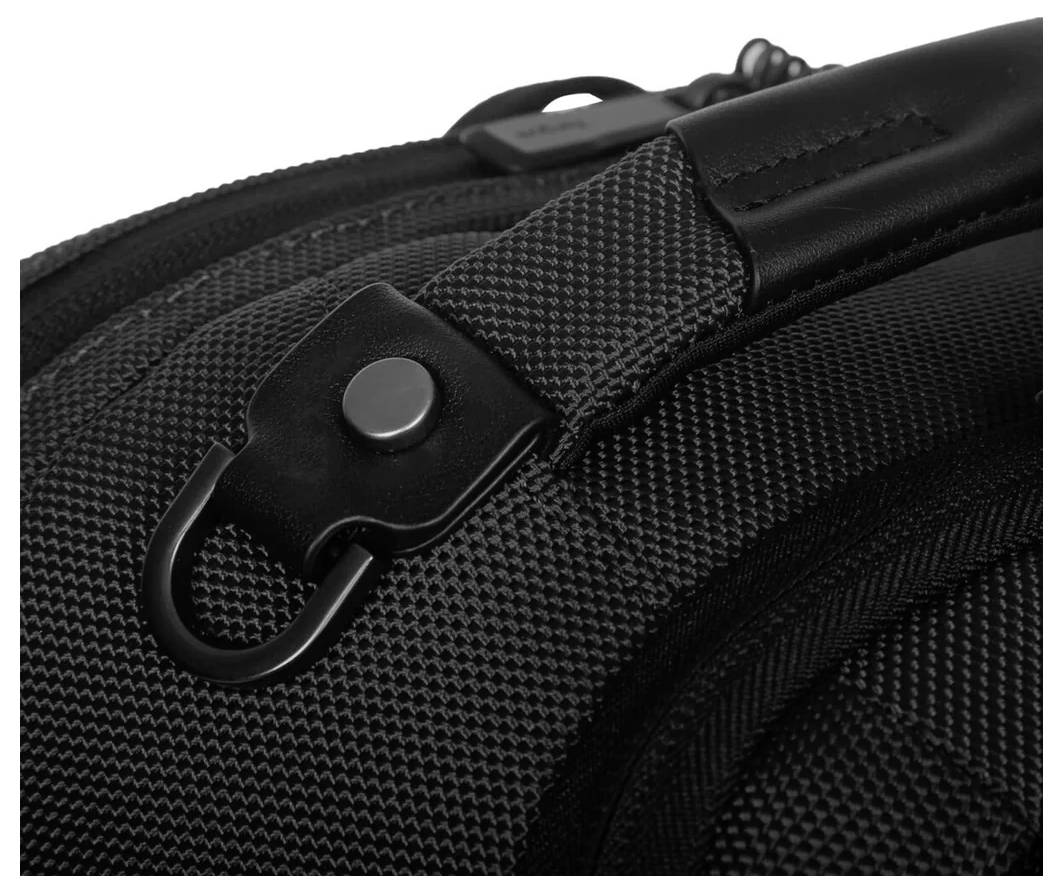 Nahaufnahme eines schwarzen Rucksacks mit texturiertem Stoff und einem Metallbeschlag mit Druckknopf an einem Riemen.