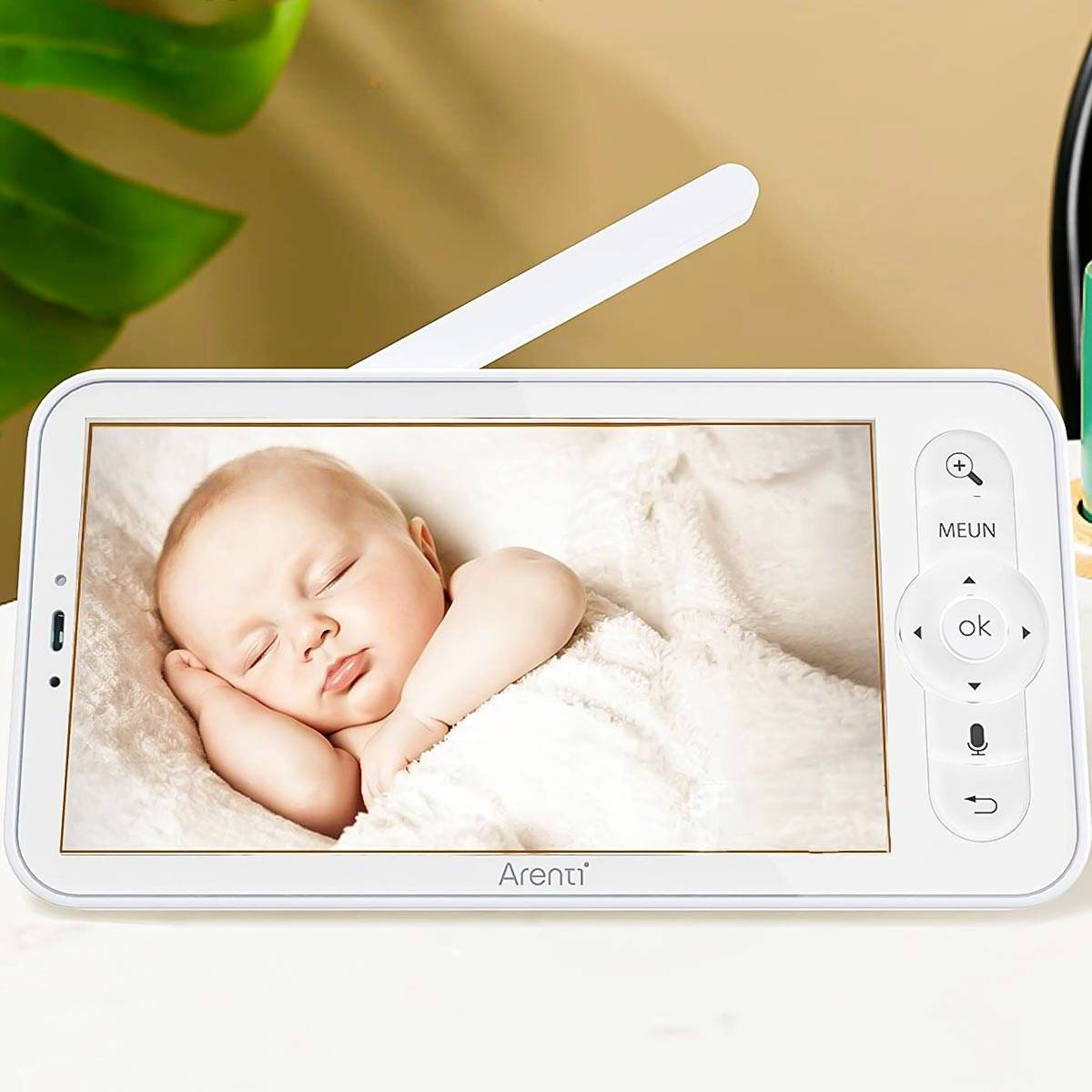 Ein Baby schläft friedlich auf einem Monitor mit Steuerknöpfen, umgeben von sanften Farben. Ein grünes Blatt ist im Hintergrund sichtbar.