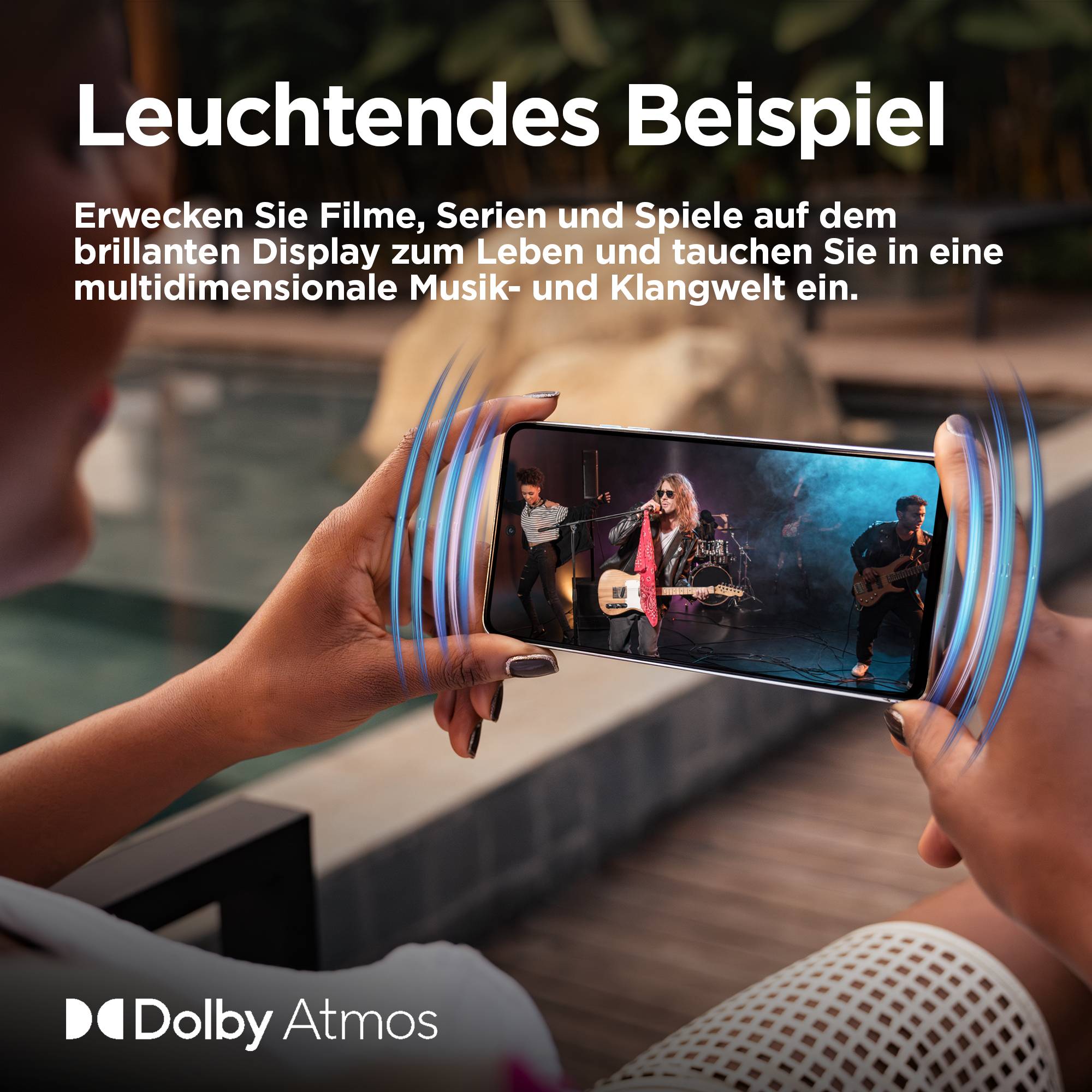 Eine Person hält ein Handy, das ein Konzert zeigt. Text: 'Leuchtendes Beispiel', beschreibt immersives Hörerlebnis mit Dolby Atmos.