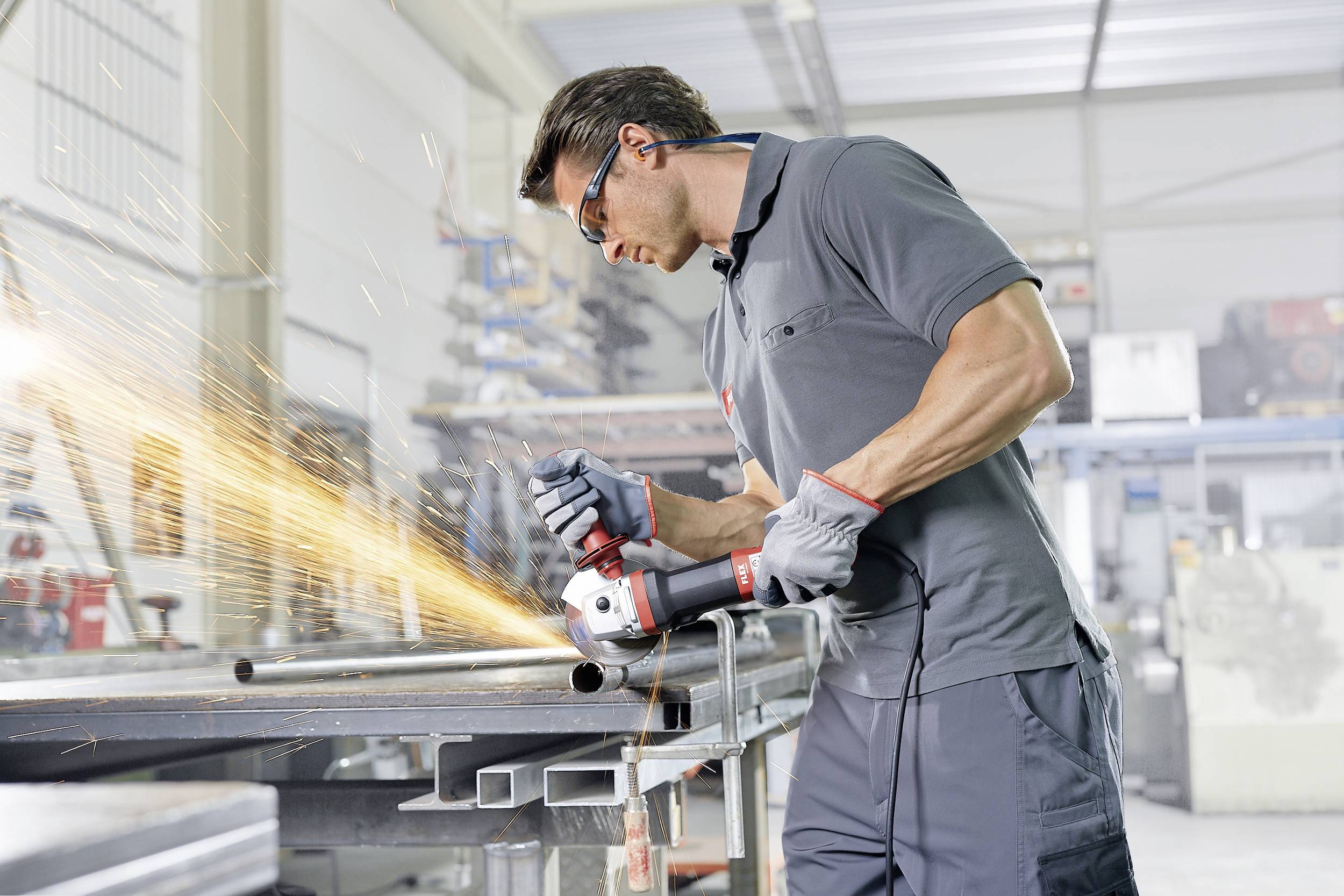 Ein Mann schleift mit einer elektrischen Schleifmaschine Metall in einer Werkstatt. Funken fliegen während des Bearbeitungsprozesses.
