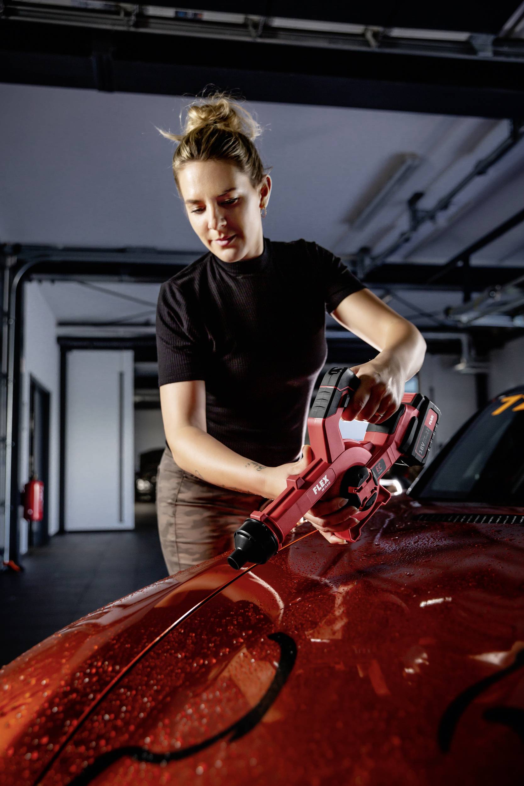Eine Person poliert mit einer roten Poliermaschine die Motorhaube eines roten Autos in einer Garage.