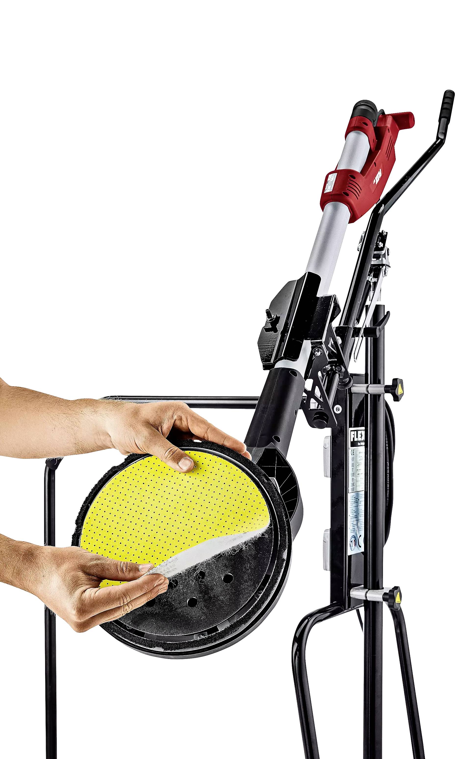 Eine Person befestigt ein gelbes Schleifpad an einer Steinschleifmaschine. Die Maschine hat einen roten Griff und ist auf einem Ständer montiert.