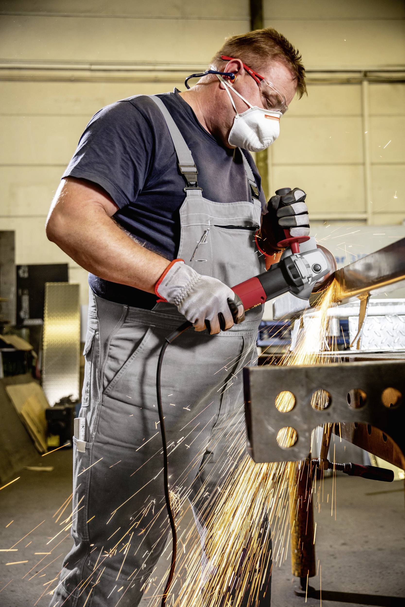Ein Arbeiter in Schutzkleidung schleift Metall mit einer Winkelschleifmaschine, Funken fliegen. Sicherheit am Arbeitsplatz ist wichtig.