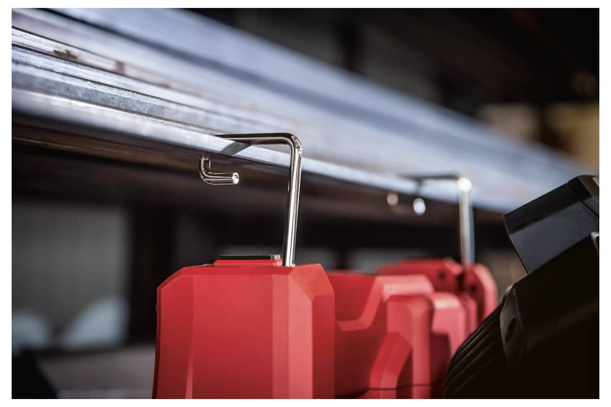 Zwei rote Kanister hängen an Metallhaken unter einem Regal. Das Bild zeigt einen Werkstatt- oder Lagerraum mit industriellem Charakter.