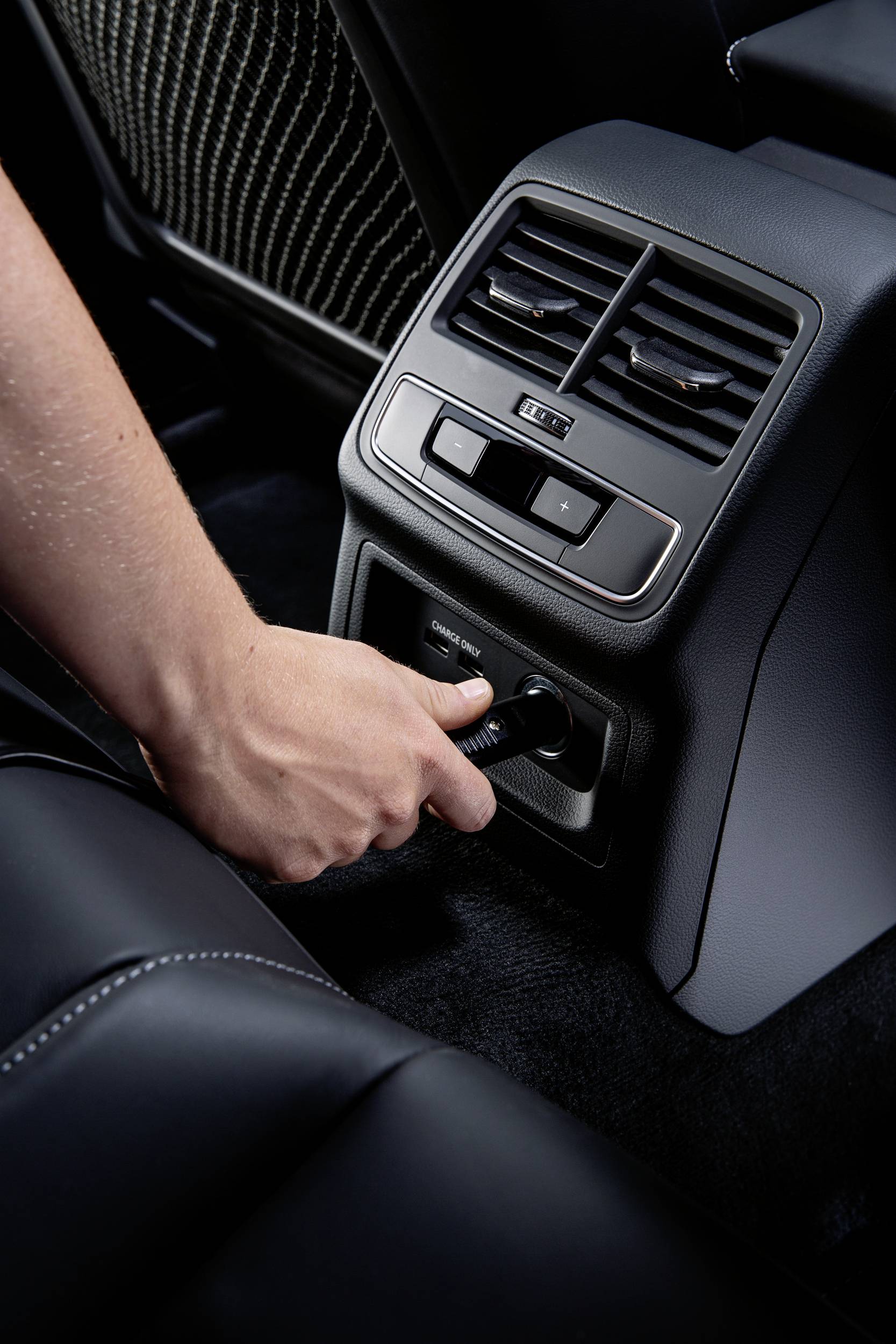 Eine Hand steckt ein Kabel in eine Steckdose im Rücksitzbereich eines Autos.