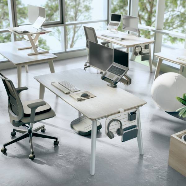 Mehrere moderne Büroschreibtische mit Laptops, Bürobedarf und ergonomischen Stühlen in einem hellen, geräumigen Raum mit großen Fenstern.
