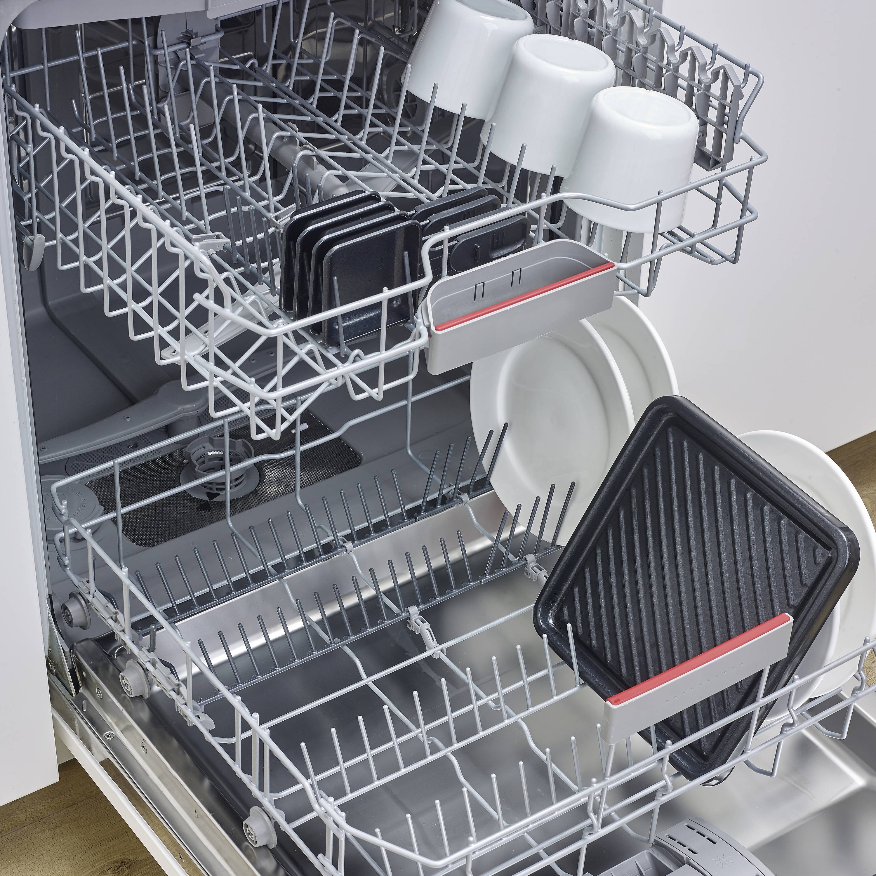 Ein geöffneter Geschirrspüler mit Geschirr: Obere und untere Ebene mit Tassen, Tellern und Tabletts. Tabletts in Bestellkästen platziert.