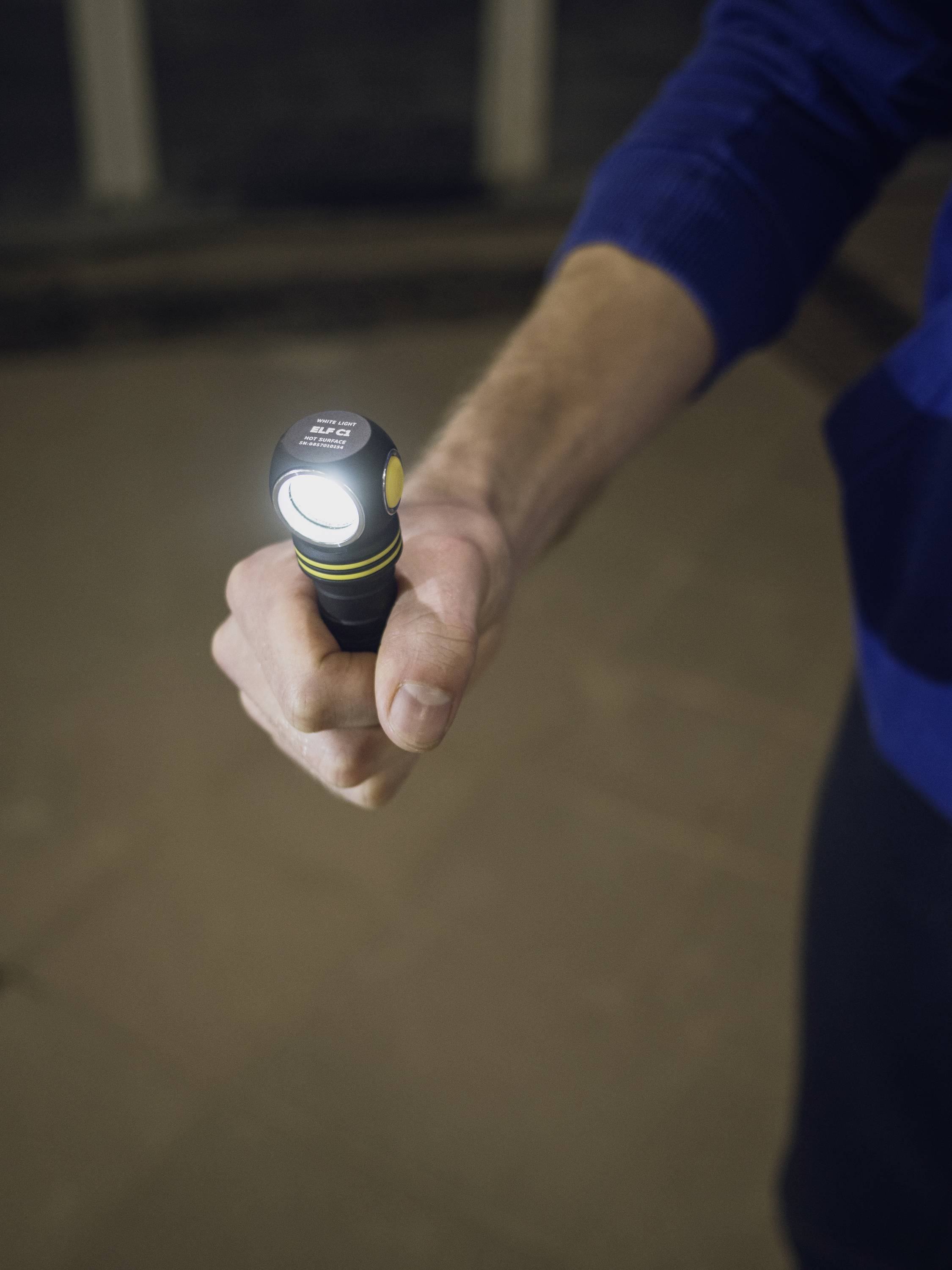 Eine Person hält eine eingeschaltete Taschenlampe in der Hand, die nach vorne leuchtet. Die Umgebung ist dunkel.