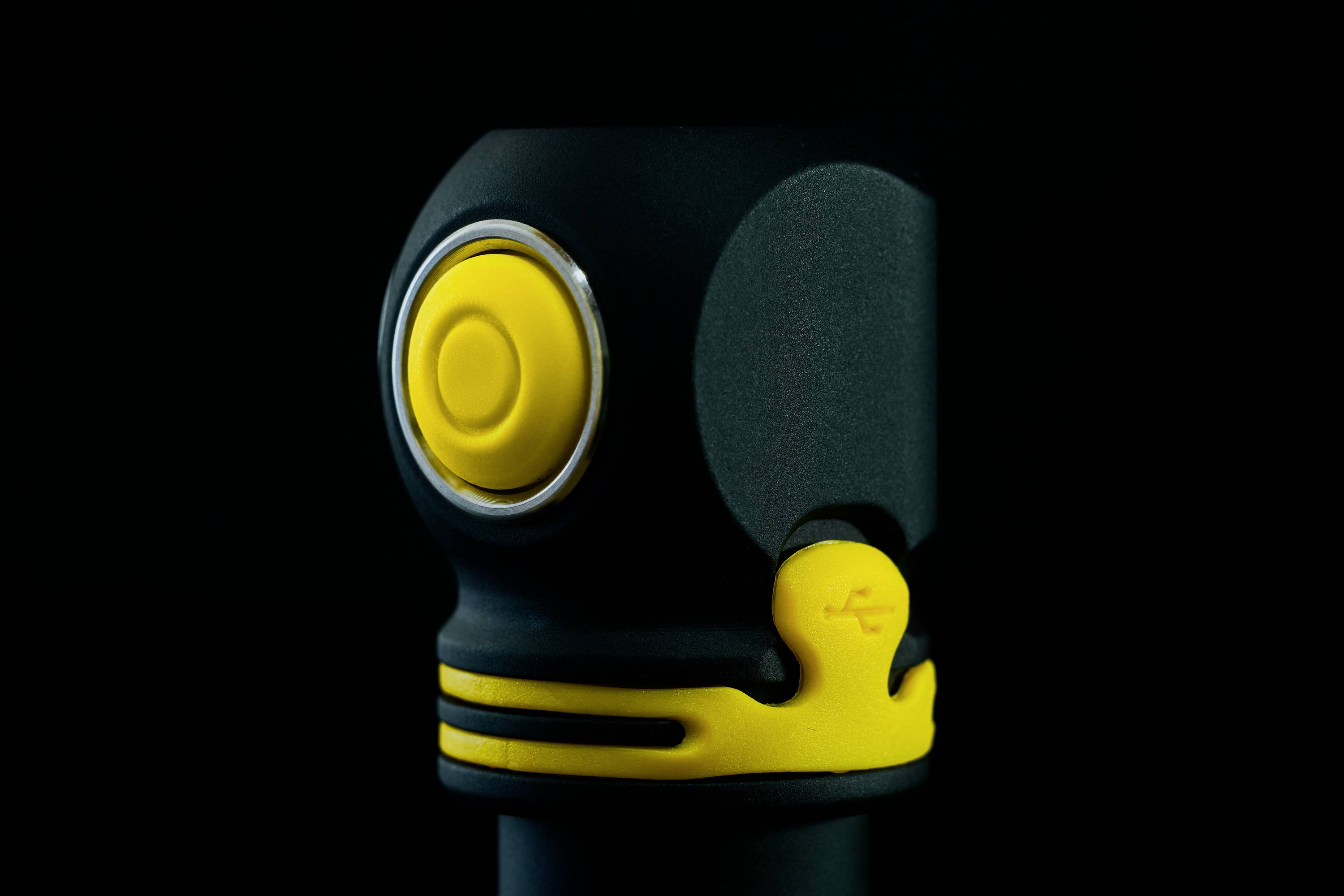 Ein schwarzes Gerät mit gelbem Knopf vor schwarzem Hintergrund. Der Knopf ist rund und von einem silbernen Ring umgeben.