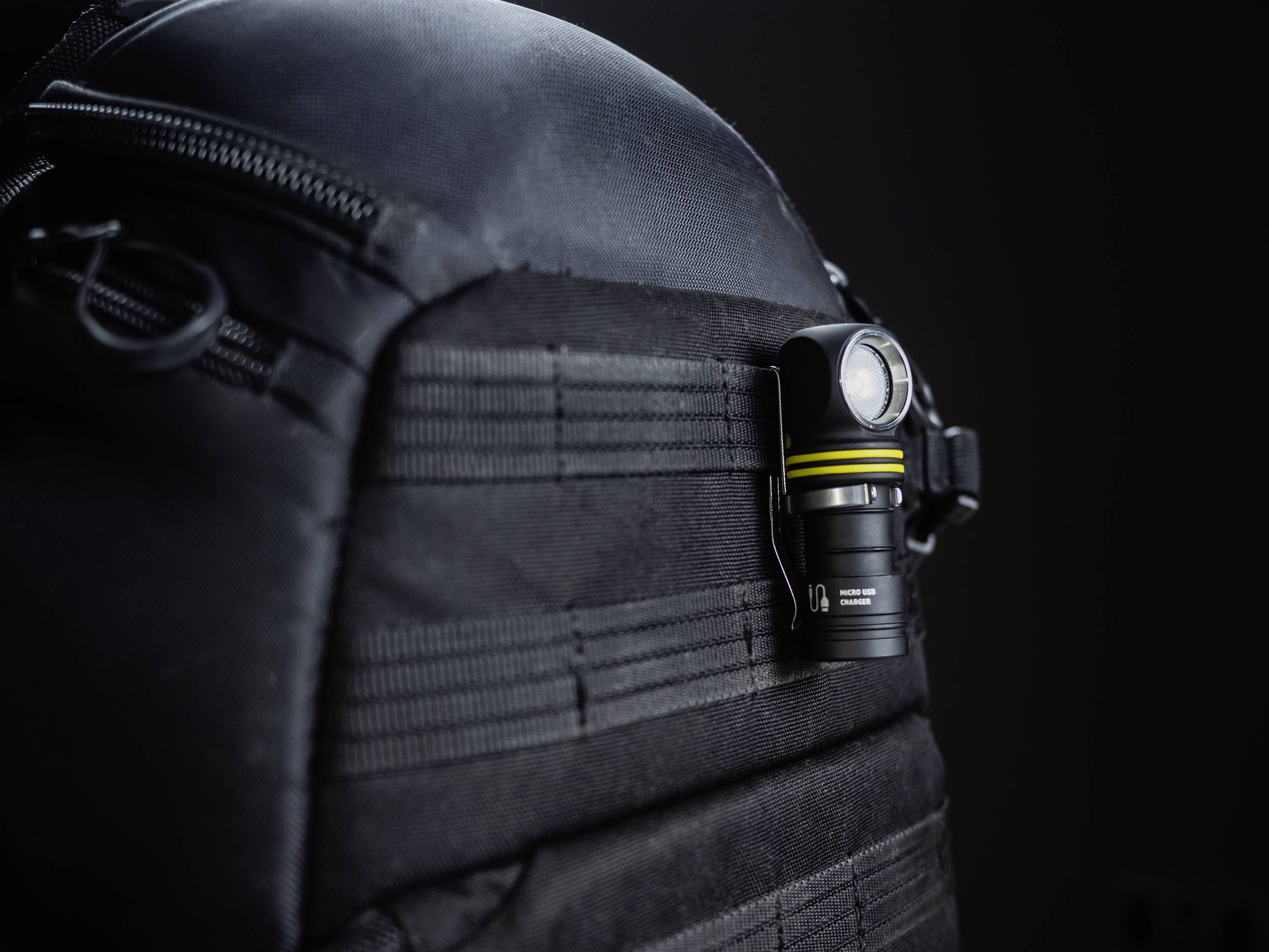 Schwarzer Rucksack mit einer kleinen Taschenlampe, die an der Seite befestigt ist. Die Szene suggeriert Ausrüstung für Outdoor-Aktivitäten.
