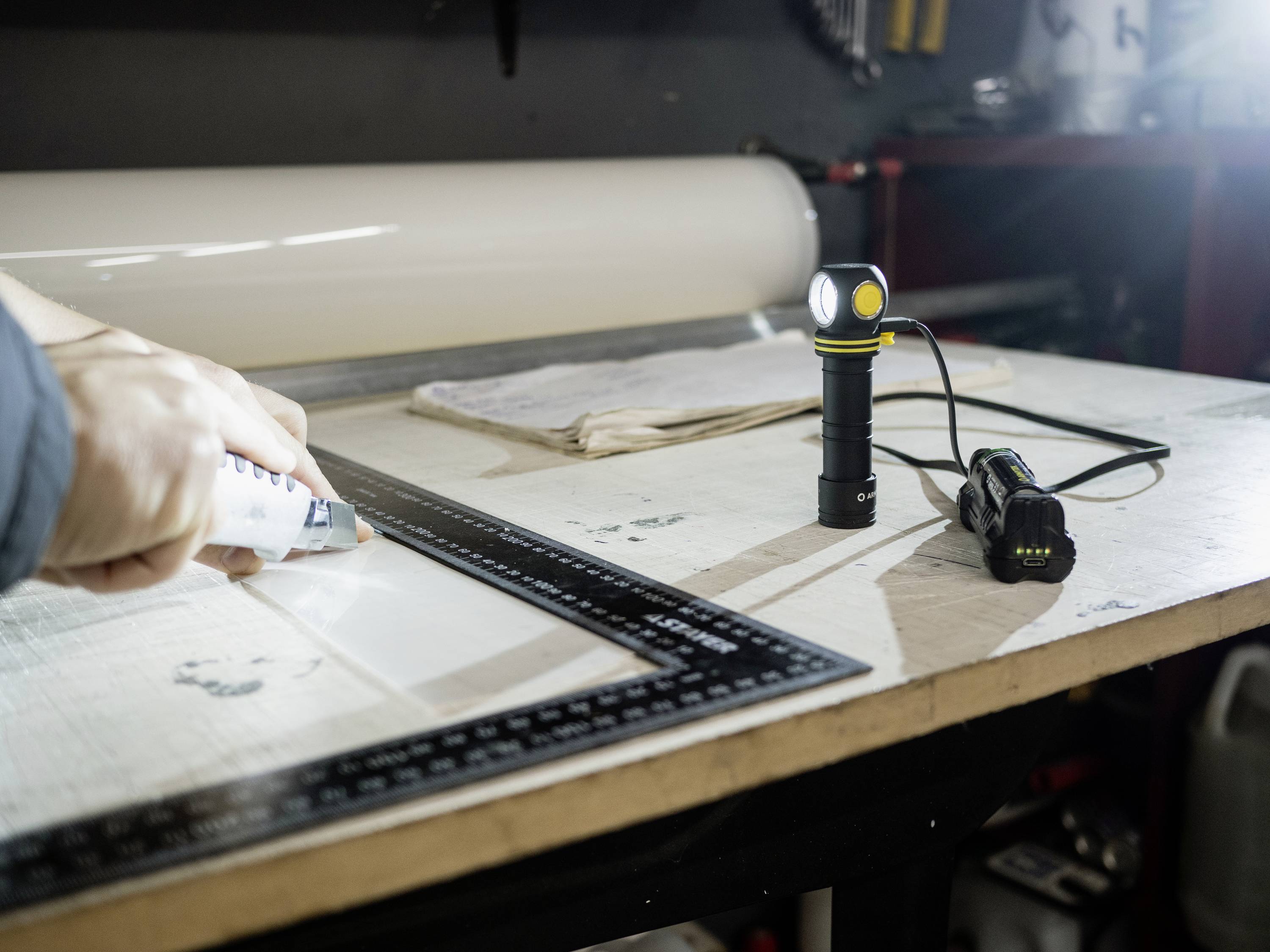 Eine Person klebt mit einer Klebepistole auf einer Arbeitsfläche. Daneben stehen eine Taschenlampe und ein Lineal, die bei der Arbeit helfen.