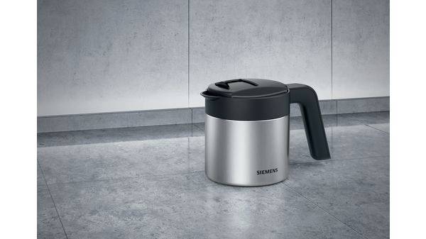 Eine silberne Teekanne mit schwarzem Griff und Deckel steht auf einem grauen Steinboden.