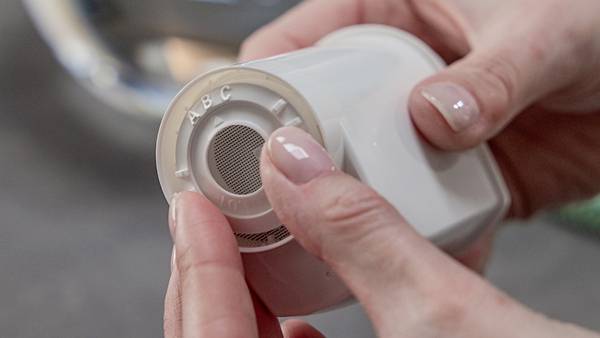 Eine Person hält einen Wasserfilter, prüft den Einsatz. Filter hat Aufschrift 'A B C'. Hände sind im Fokus, Hintergrund unscharf.