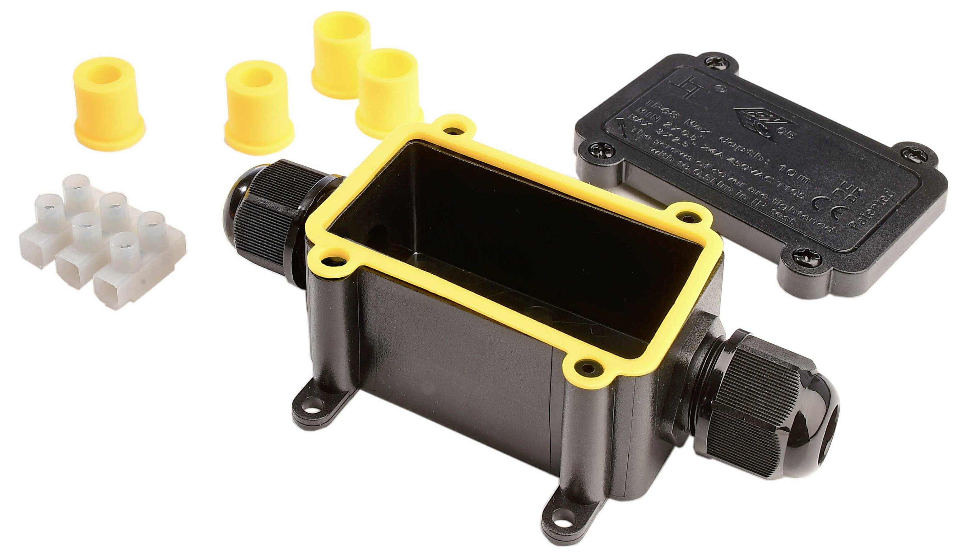 Schwarze Anschlussdose mit gelbem Rand und Kabelverschraubungen, abgenommenem Deckel. Enthält Zubehör: Gelbe Gummiverschlüsse und weiße Klemmleiste.