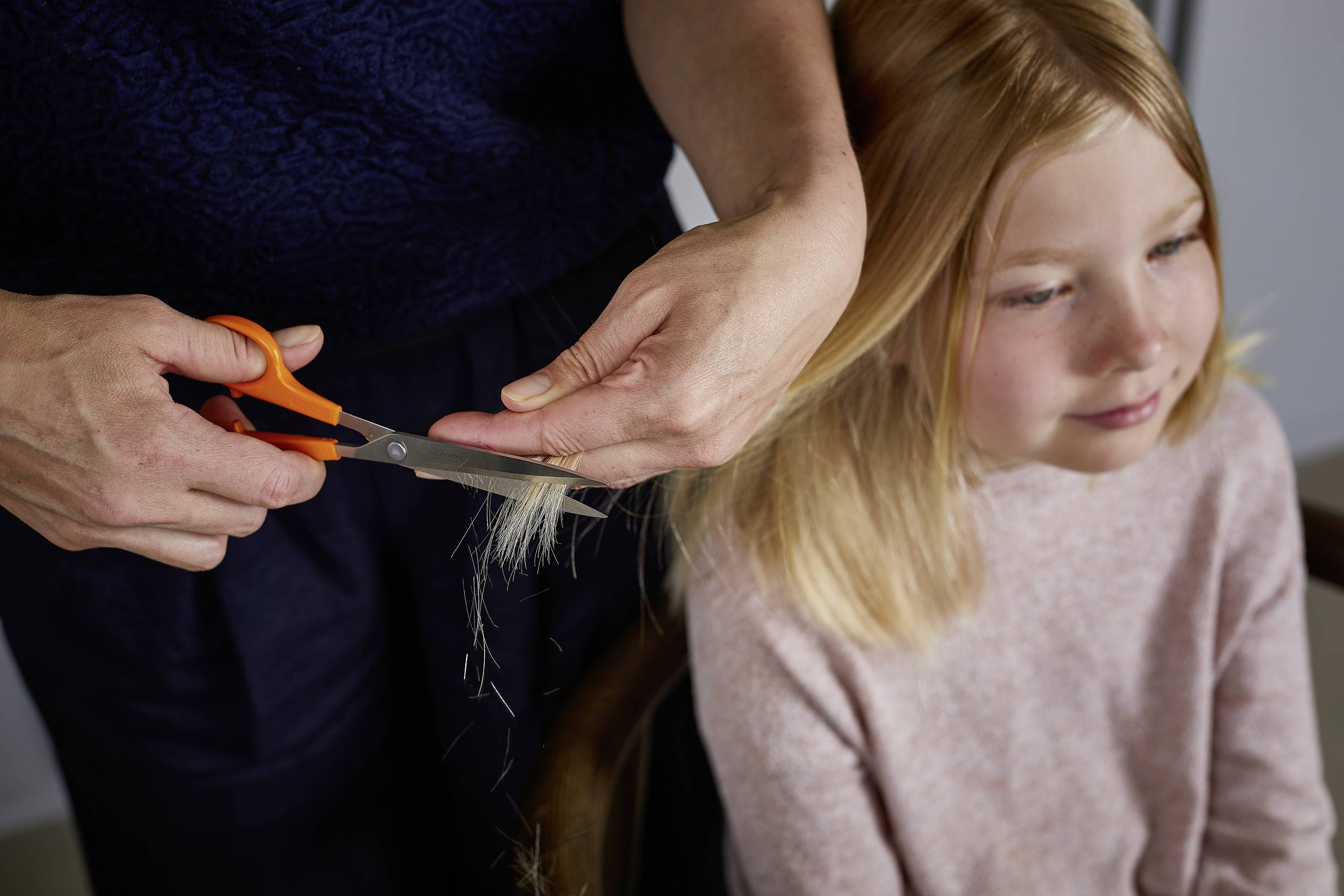 Ein Kind sitzt, während eine Person sein blondes Haar mit einer Schere schneidet.