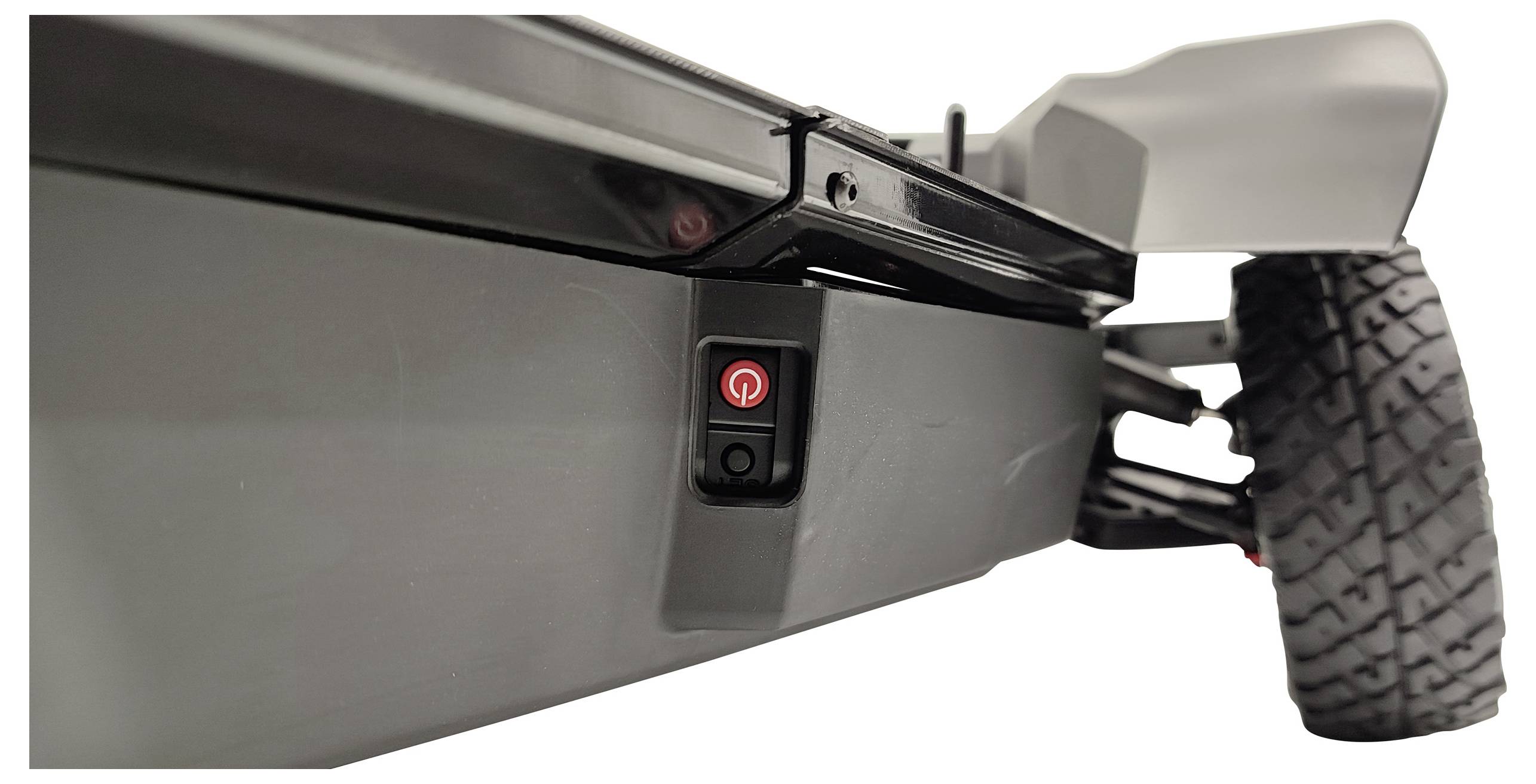 Unterseite eines Rasenmähers mit einem roten Ein-/Ausschalter. Ein Rad und Teil des Gehäuses sind sichtbar.