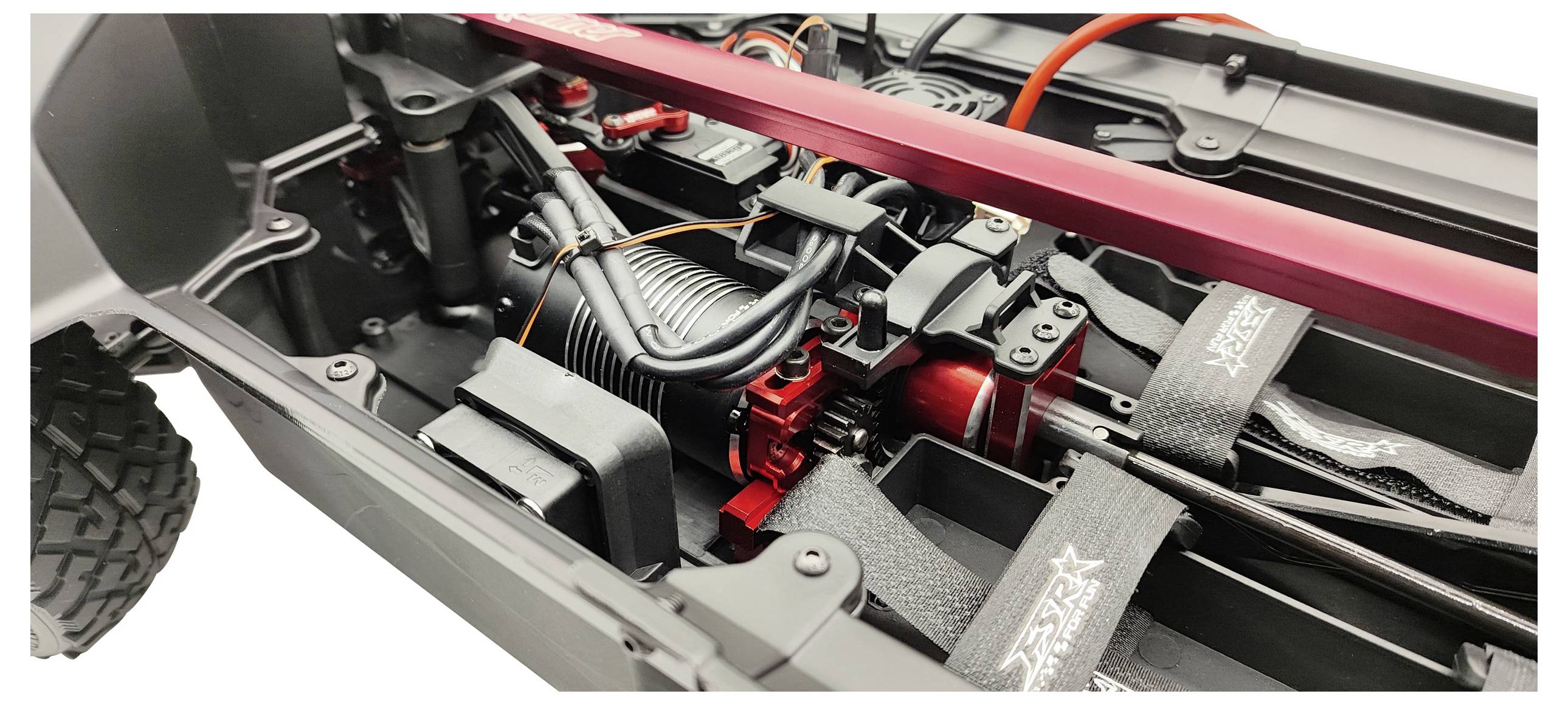 Nahaufnahme eines ferngesteuerten Autos mit Fokus auf dem Motor, Verkabelung und Federungselementen im Chassis. Dynamisches Design erkennbar.