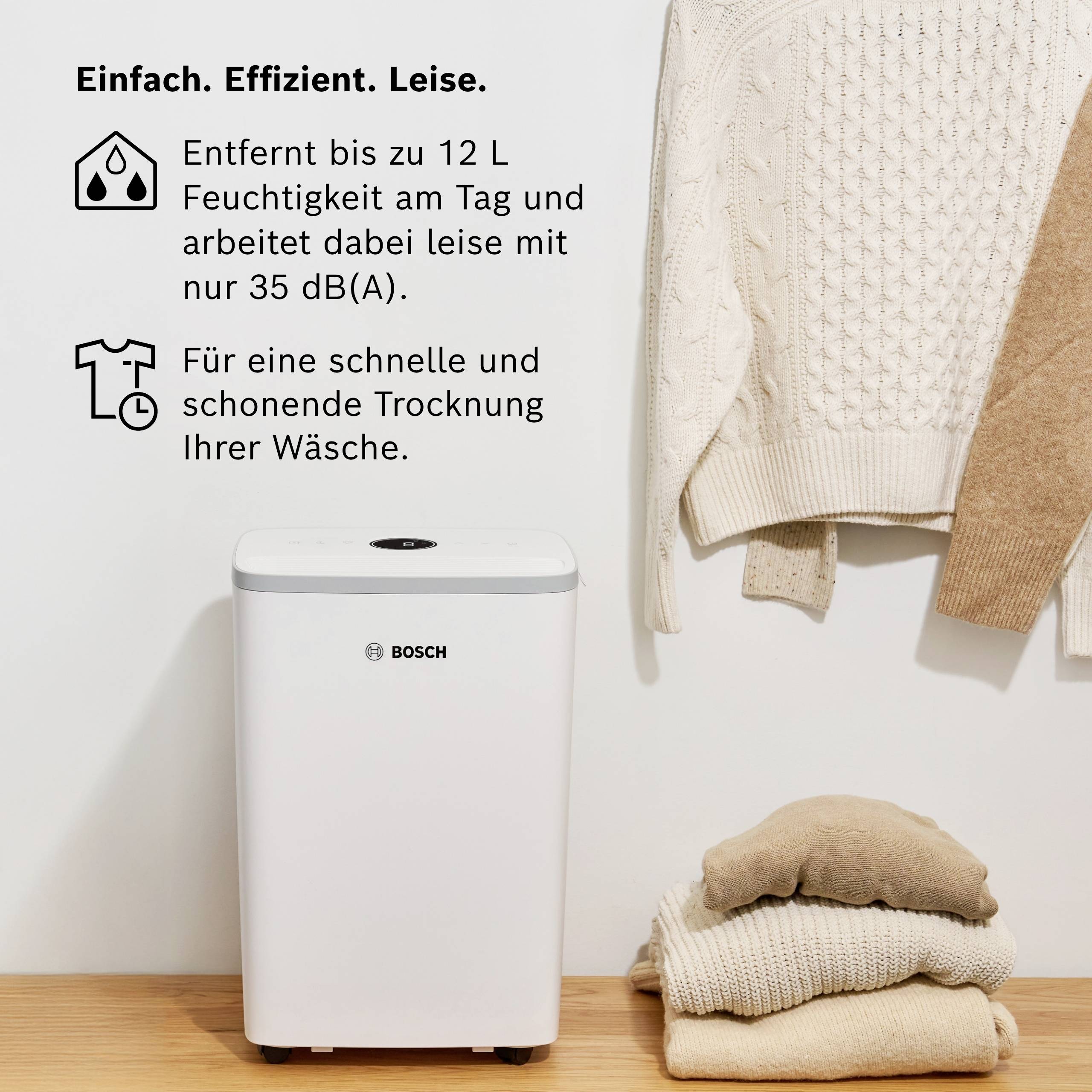 Entfeuchter von Bosch neben Handtüchern und Pullover; entfernt 12 L Feuchtigkeit pro Tag, arbeitet leise bei 35 dB, schont Wäsche.