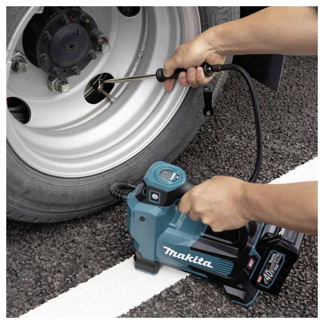 Eine Person bläst einen Fahrzeugreifen mit einem tragbaren Makita-Luftkompressor auf einer Straße auf. Der Kompressor zeigt die Markenbezeichnung „40V max