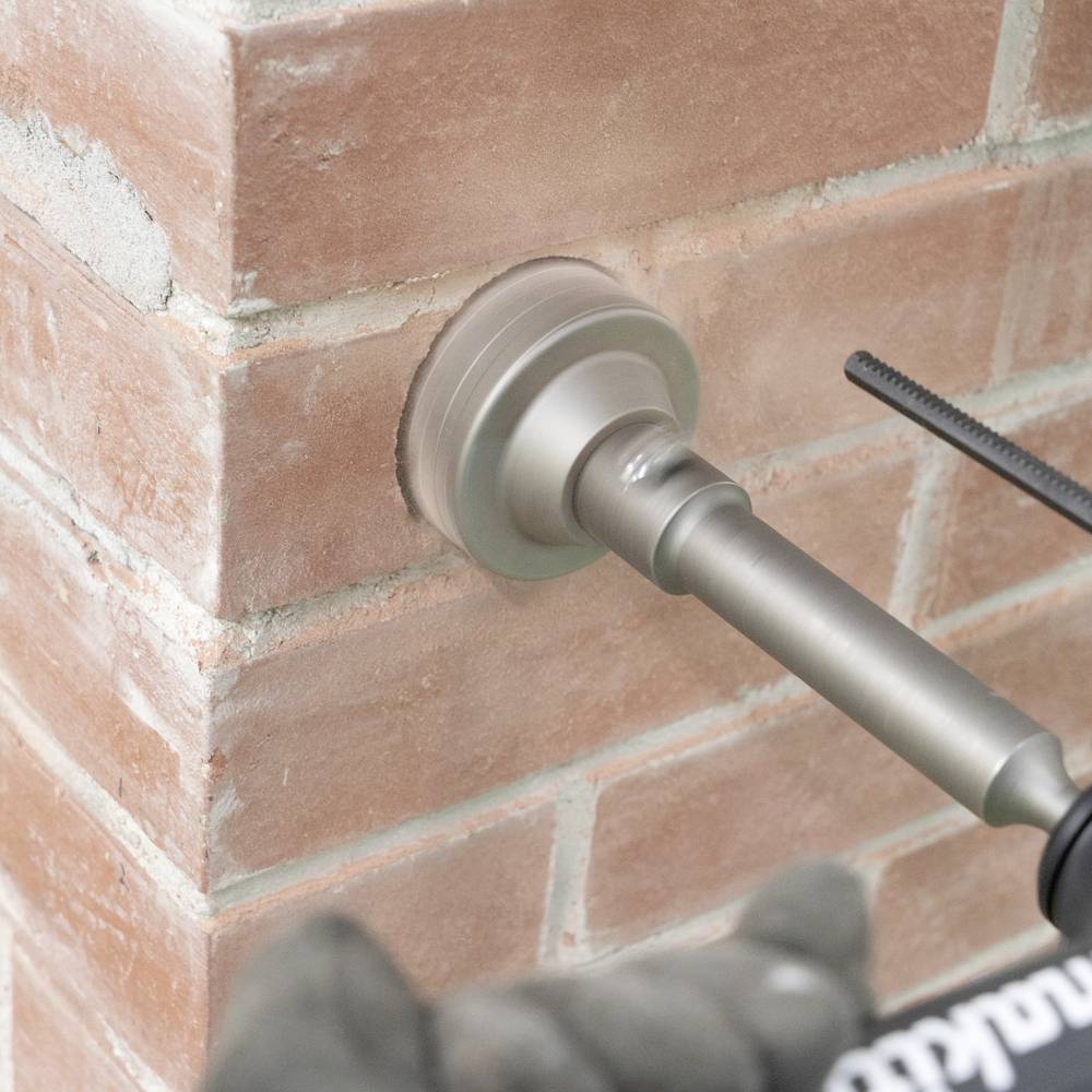 Ein Bohrer, der ein Loch in eine Ziegelmauer bohrt, mit Nahaufnahmefokus auf den Bohrmeißel und die Mauer.