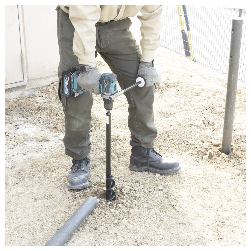 Ein Arbeiter bohrt mit einem Elektroerdbohrer ein Loch in den Boden auf einer Baustelle, wobei er Handschuhe und Stiefel trägt.
