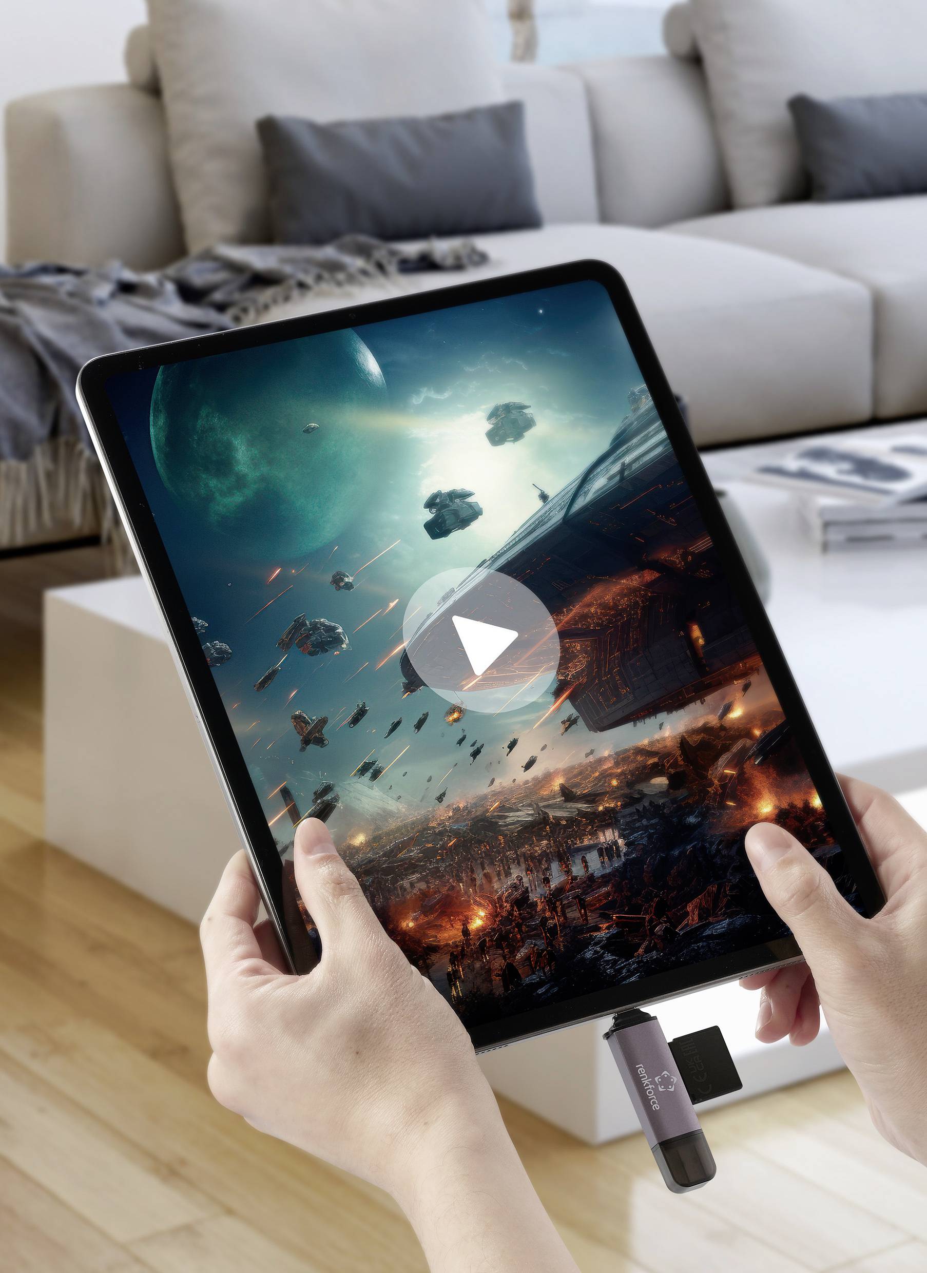 Ein Tablet, das ein Weltraum-Kampfspiel zeigt, wird von zwei Händen gehalten. Im Hintergrund ist ein Wohnzimmer mit einem Sofa sichtbar.