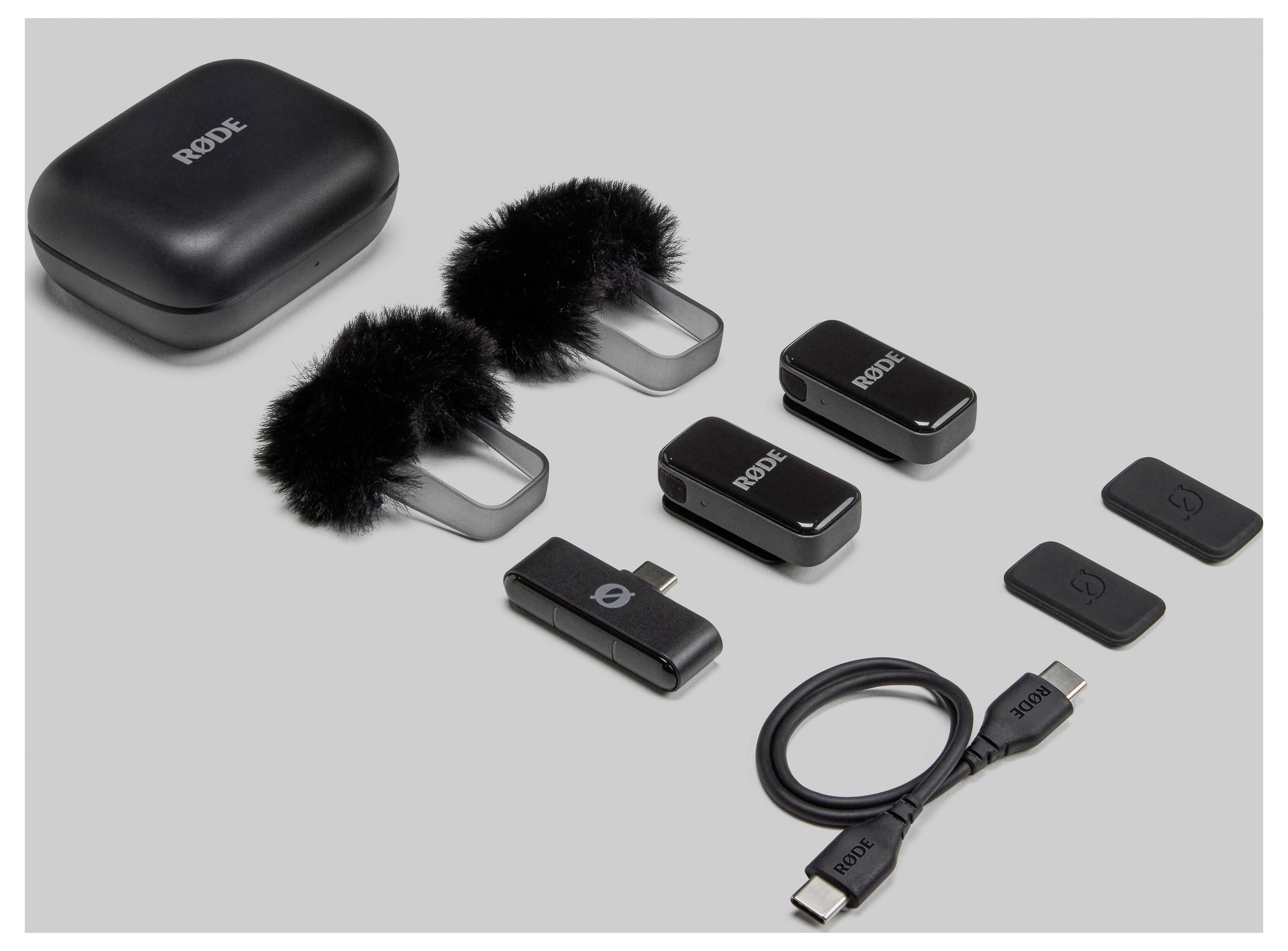 Draufsicht eines vollständigen drahtlosen Mikrofonsystems mit Ladeetui, Mikrofonen, Windschutz, Empfänger, Kabel und Adapter auf grauem Hintergrund.