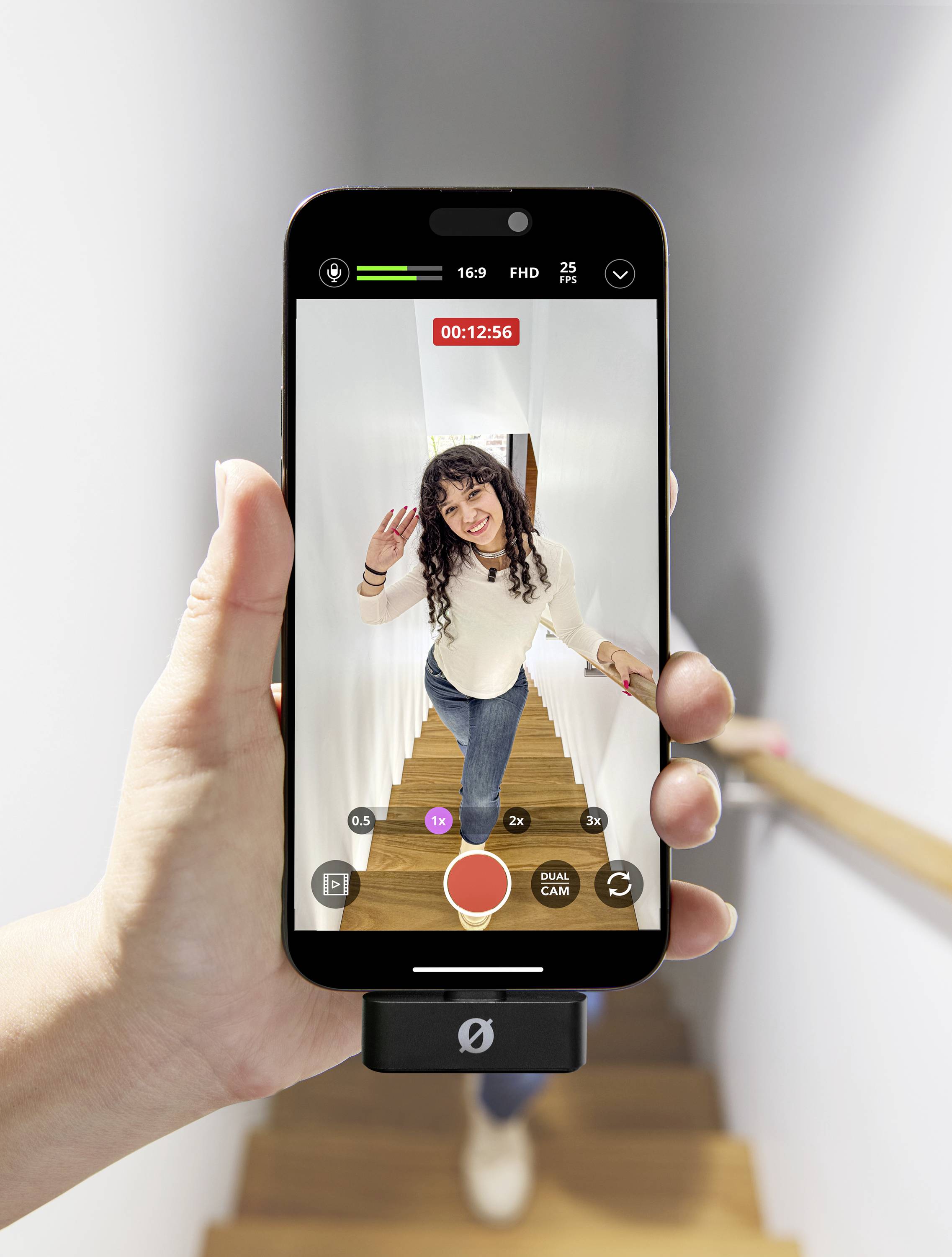 Eine Person steht auf einer Treppe und winkt in die Kamera eines Smartphones, das in der Hand gehalten wird. Auf dem Bildschirm läuft eine Videoaufnahme.