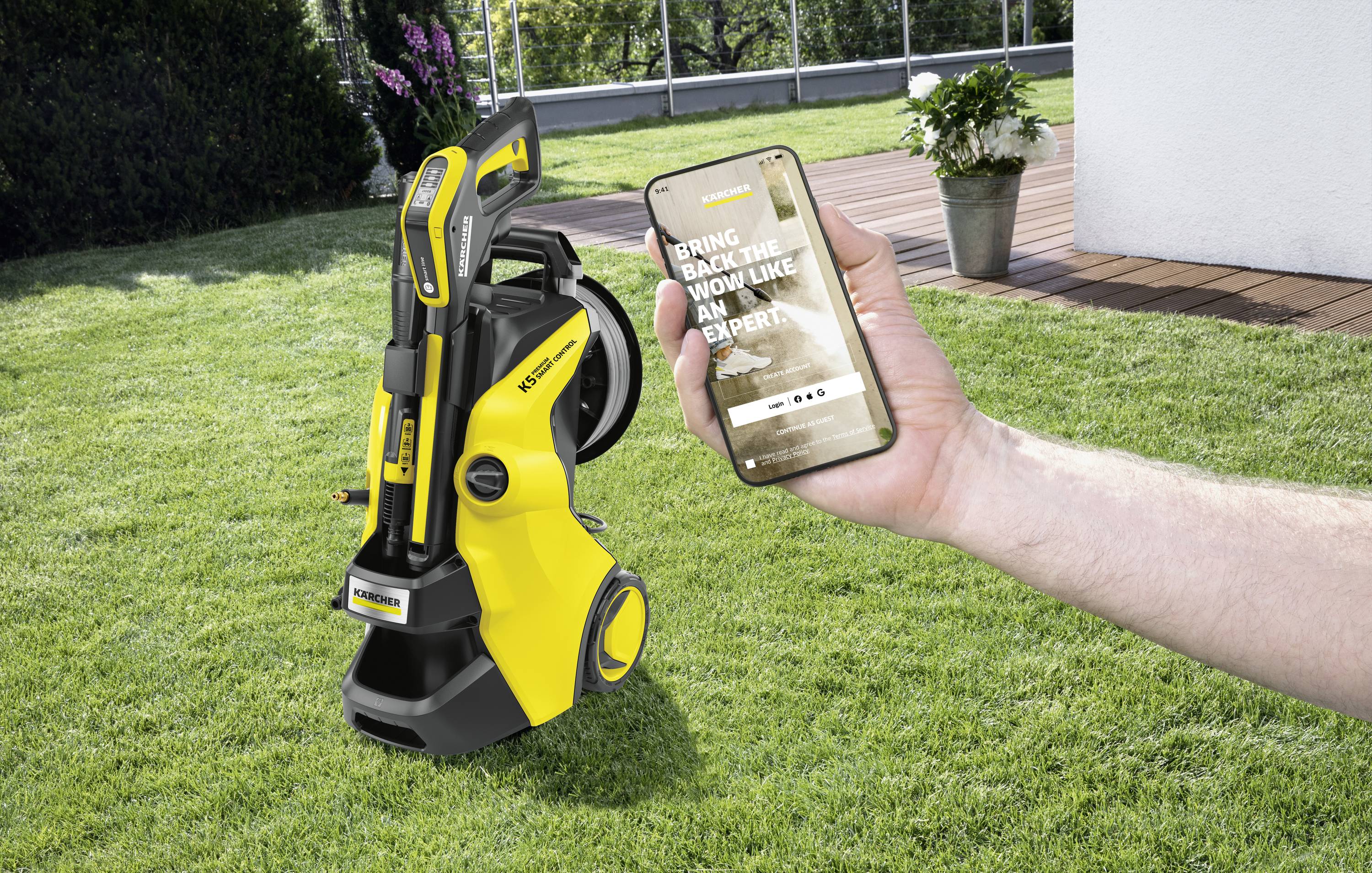 Ein gelber Hochdruckreiniger steht auf einem Rasen. Eine Hand hält ein Smartphone, auf dem eine Anzeige des Reinigers gezeigt wird.