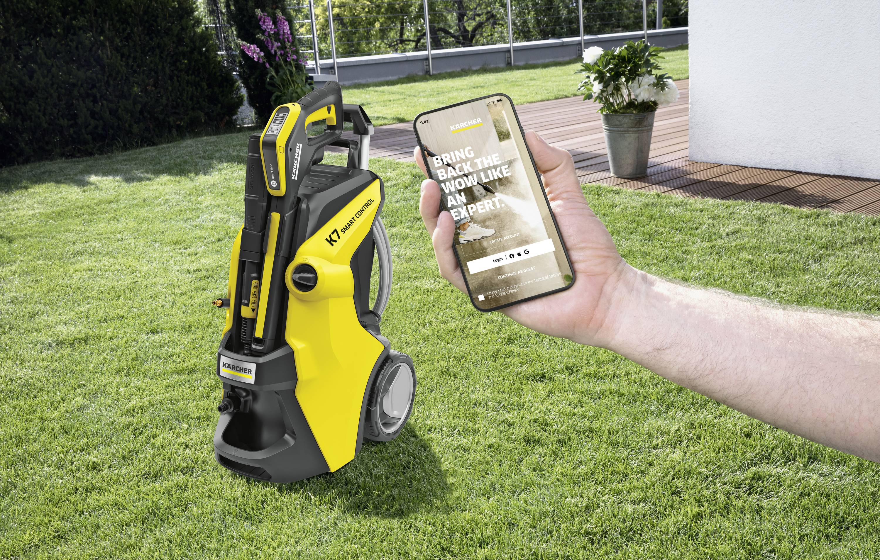 Ein Hochdruckreiniger steht auf einer Rasenfläche. Eine Hand hält ein Smartphone, das eine App für den Hochdruckreiniger zeigt.