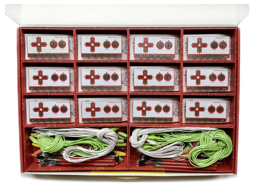 'Makey Makey'-Sets in einer Box, die mehrere Controller-Platinen und Kabel zeigen, die für Bildungsprojekte oder MINT-Aktivitäten organisiert sind.