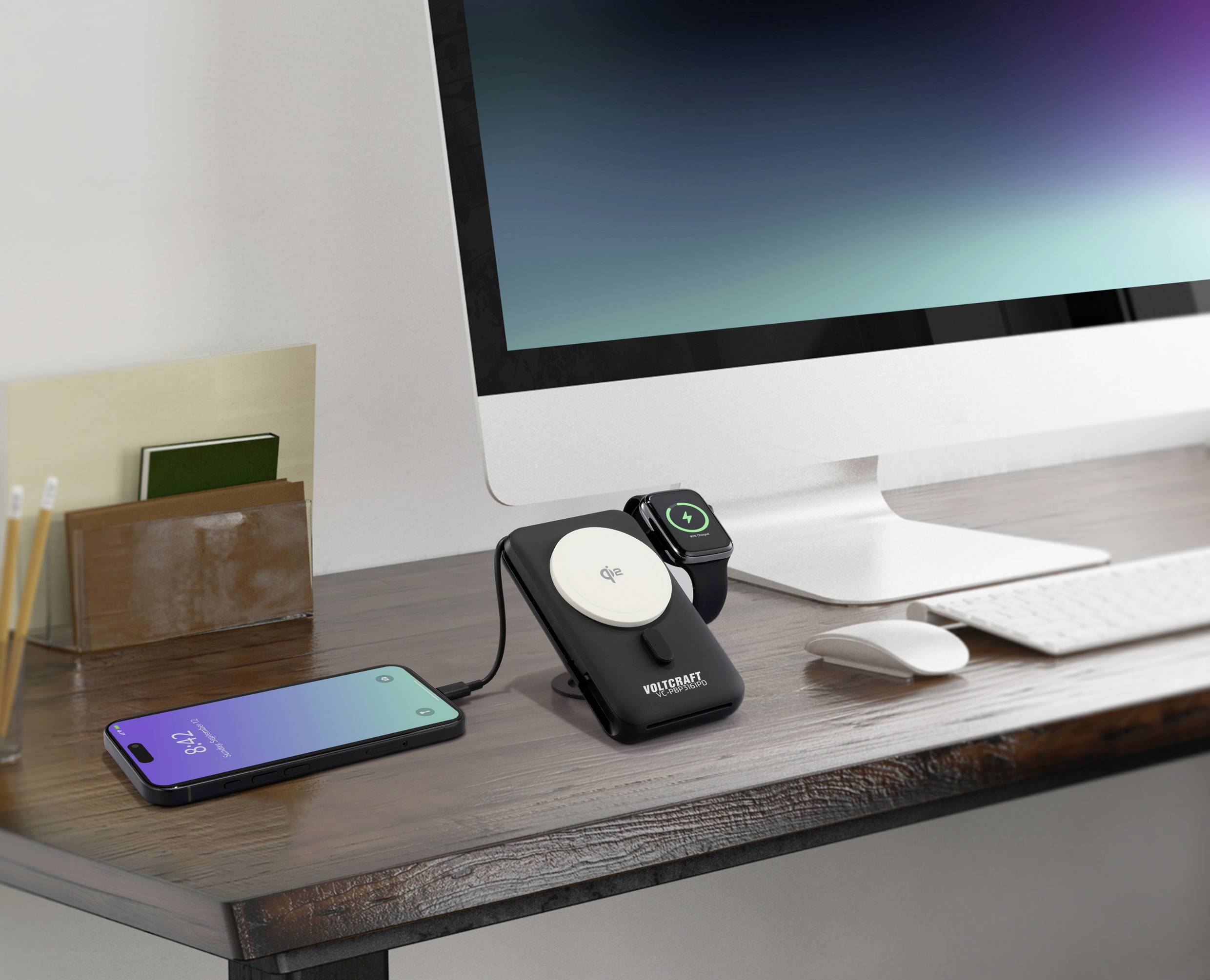 Ein Schreibtisch mit einem Computer, einem drahtlosen Ladegerät, auf dem ein Smartphone und eine Smartwatch liegen. Im Hintergrund ein Monitor.