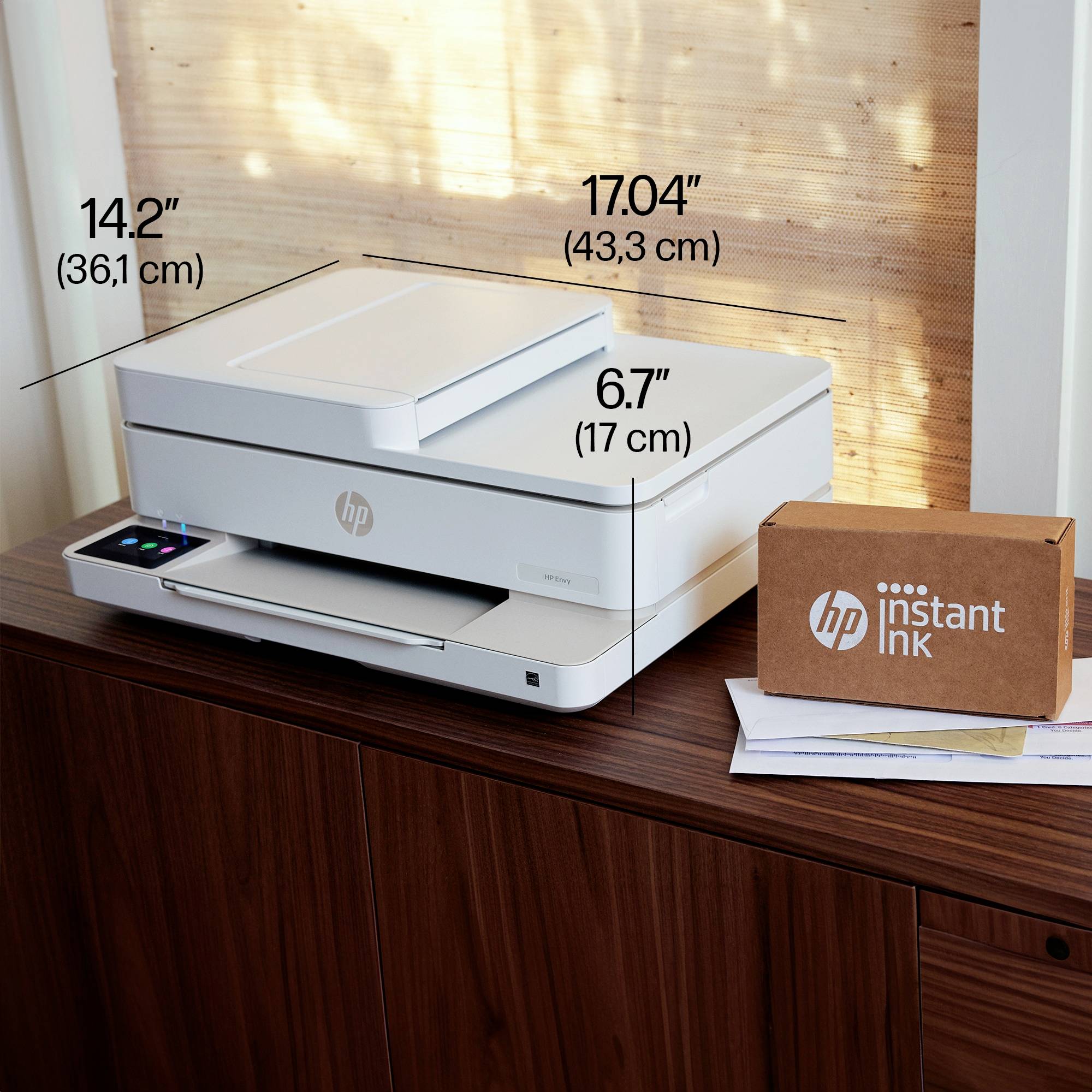 Ein Drucker steht auf einem Holztisch. Daneben liegt eine Box mit 'HP Instant Ink'-Aufdruck. Maße des Druckers sind angegeben.