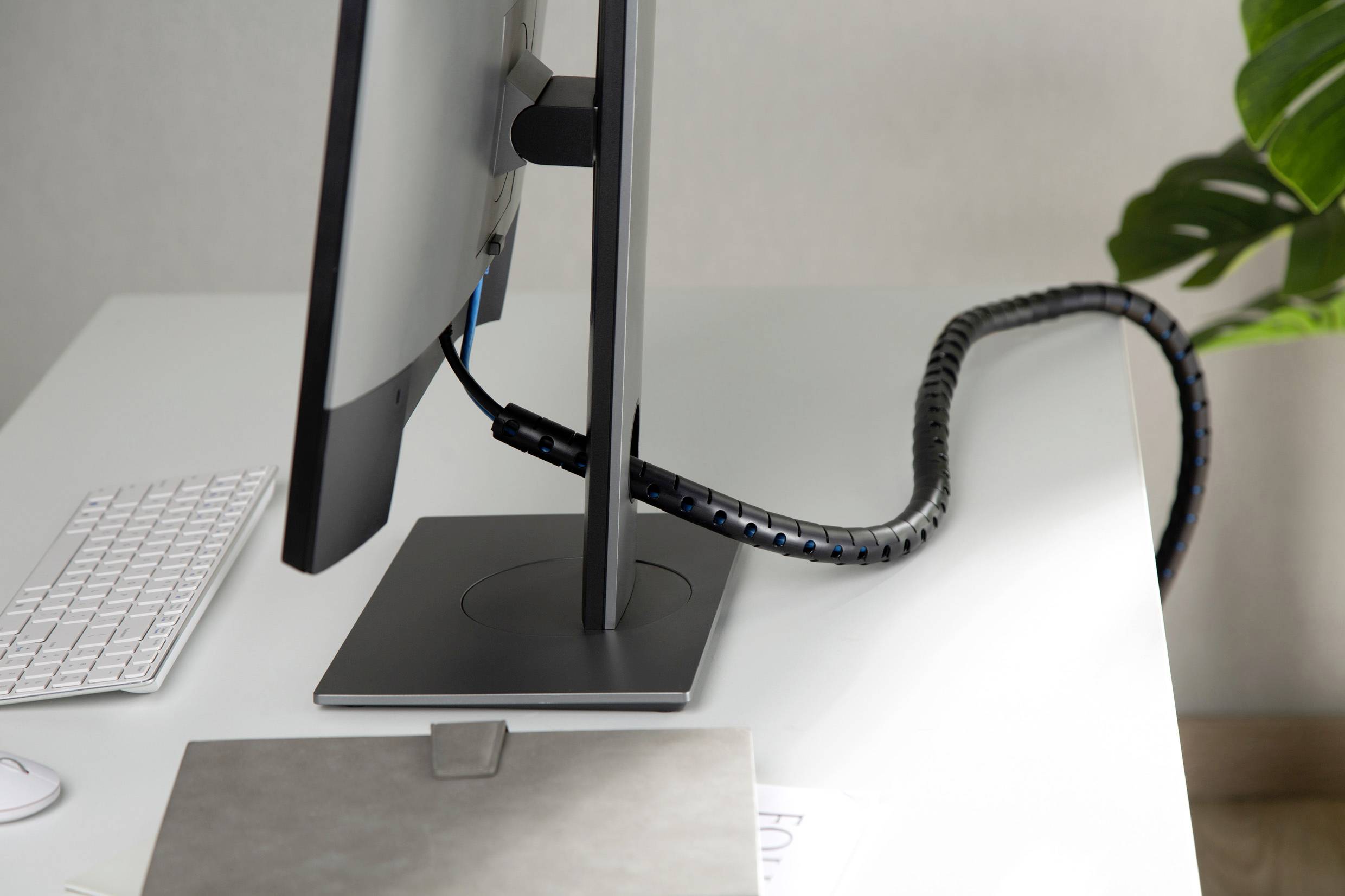 Ein Monitor auf einem Schreibtisch mit organisierten Kabeln. Daneben liegen eine weiße Tastatur und ein Laptop.