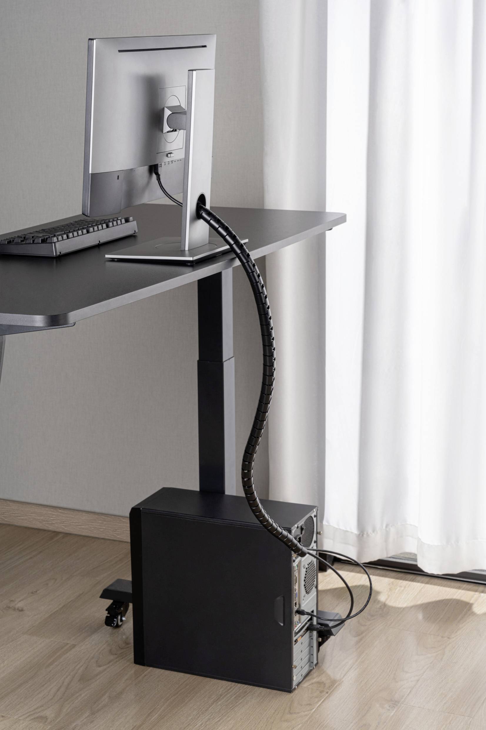 Ein Schreibtisch mit höhenverstellbarer Funktion. Ein Computer mit Monitor ist darauf platziert. Kabel sind ordentlich verlegt.